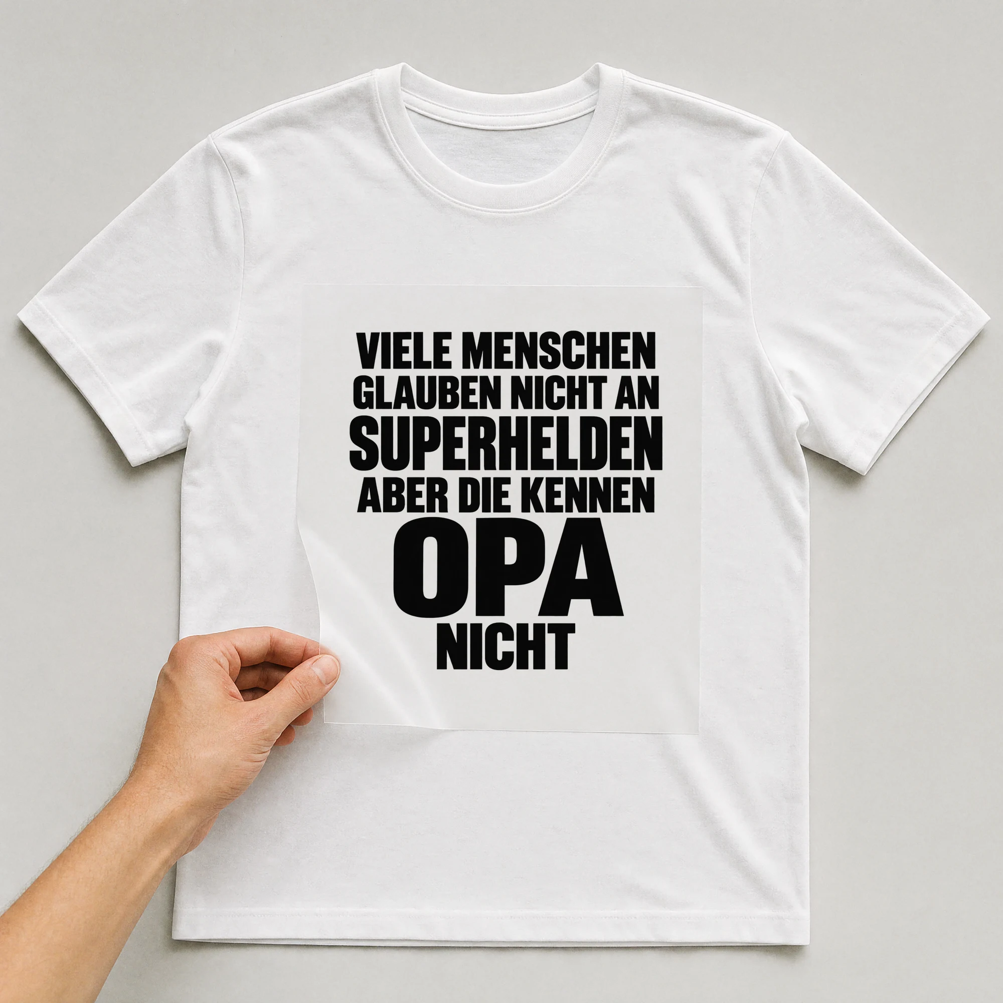 Bügelbild „Viele Menschen glauben nicht an Superhelden aber die kennen Opa nicht“ auf weißem T-Shirt, Folie wird aufgelegt