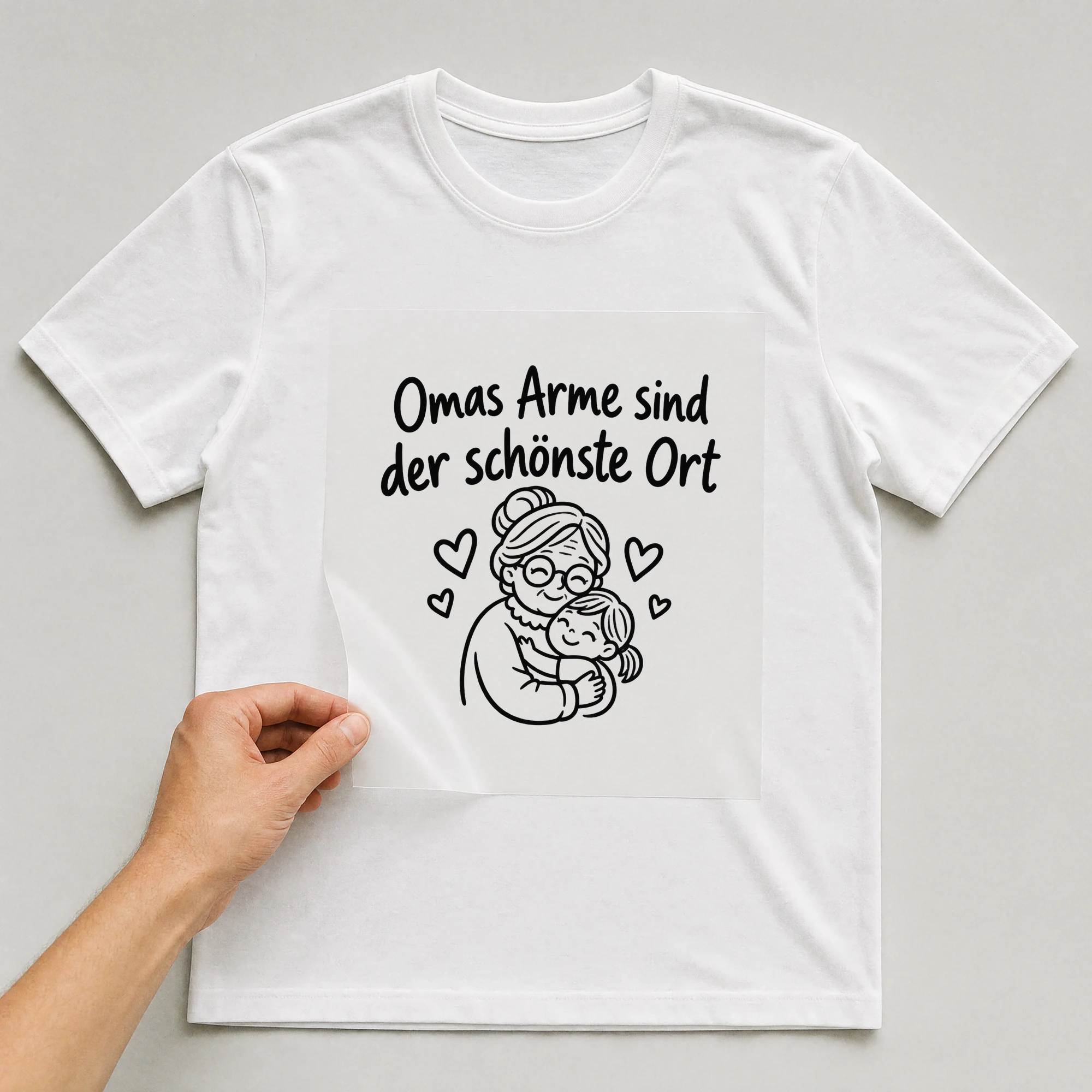 Bügelbild „Omas Arme sind der schönste Ort“ auf weißem T-Shirt, Folie wird aufgelegt