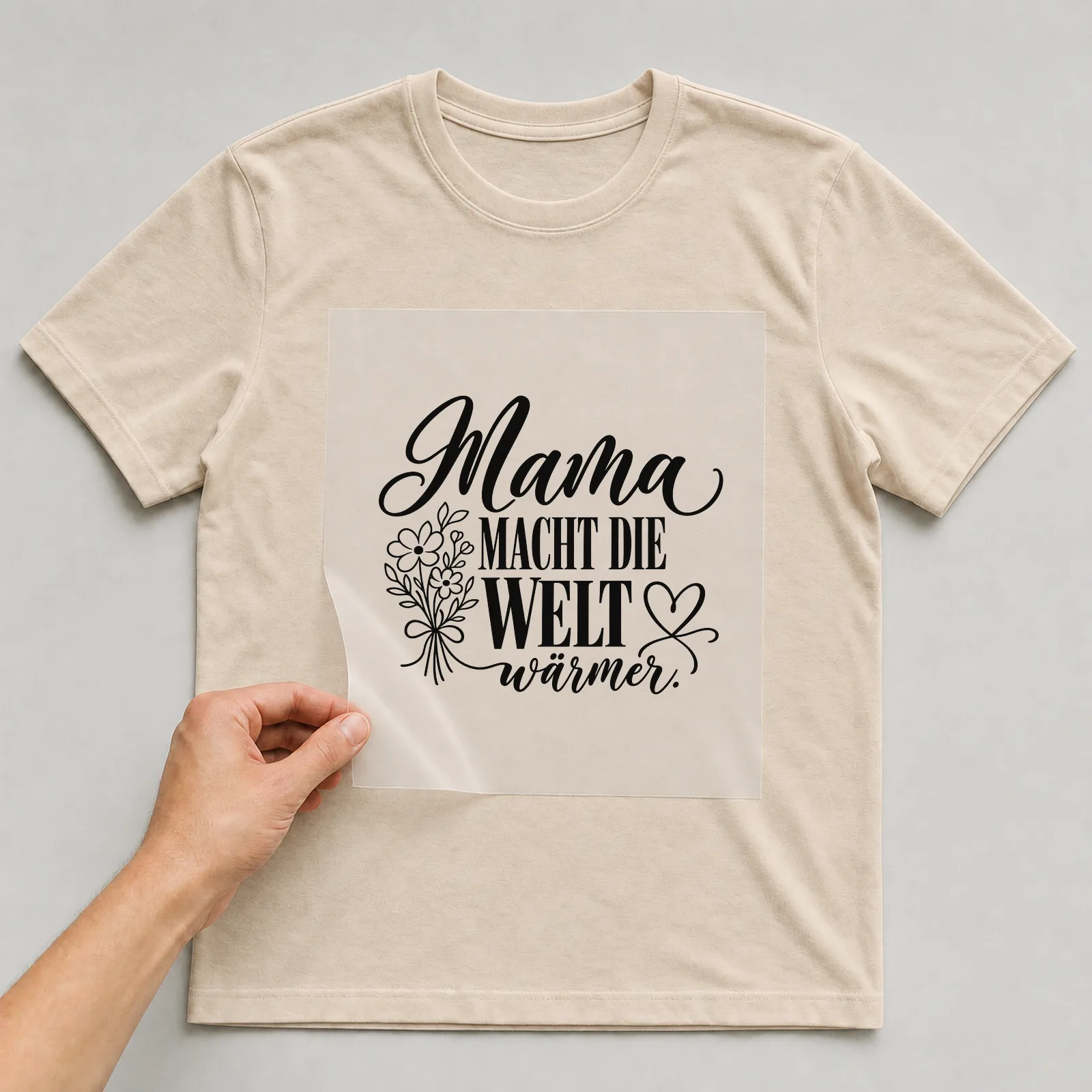 Bügelbild „Mama macht die Welt wärmer“ auf beigem T-Shirt, Folie wird aufgelegt