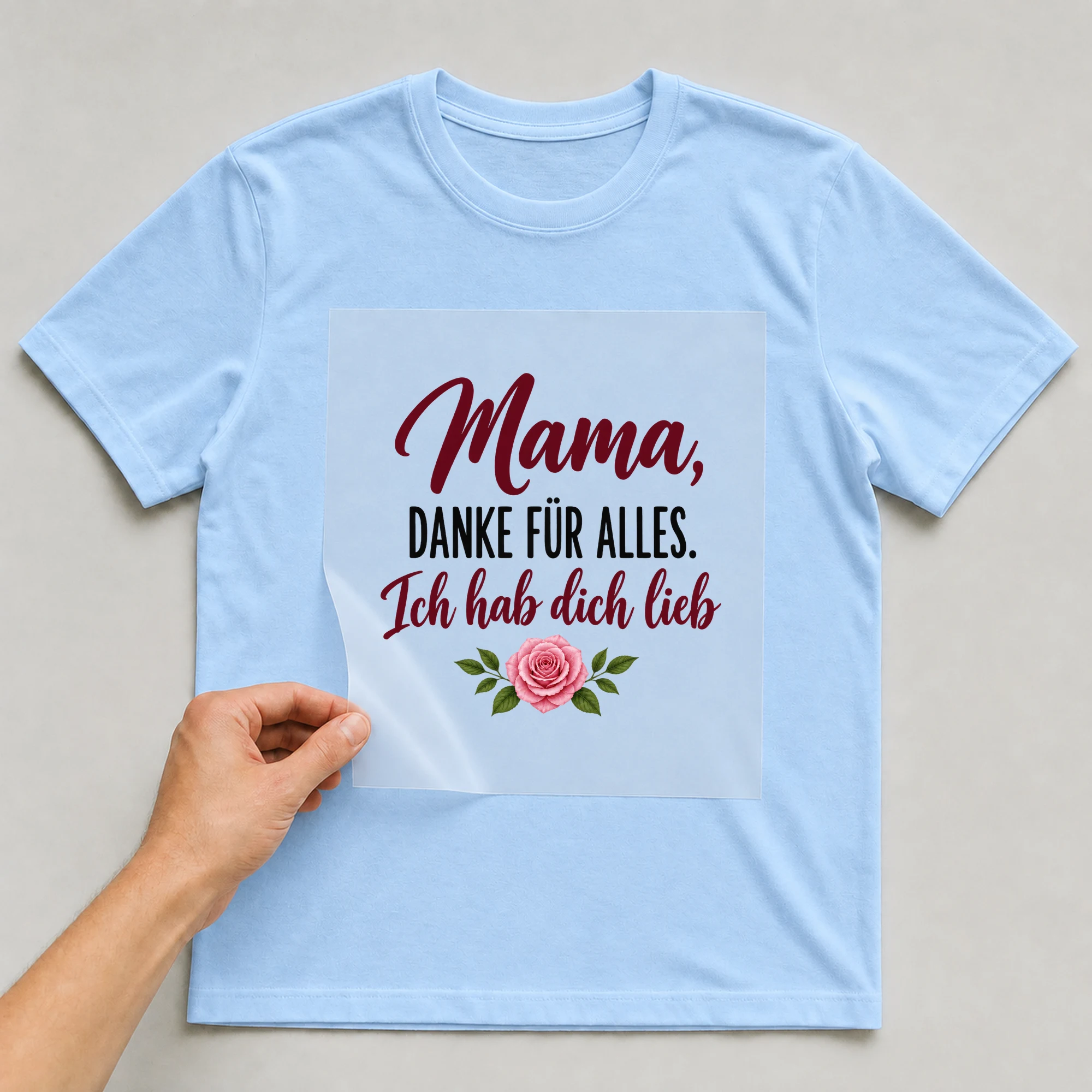 Bügelbild „Mama, danke für alles. Ich hab dich lieb.“ auf babyblauem T-Shirt, Folie wird aufgelegt