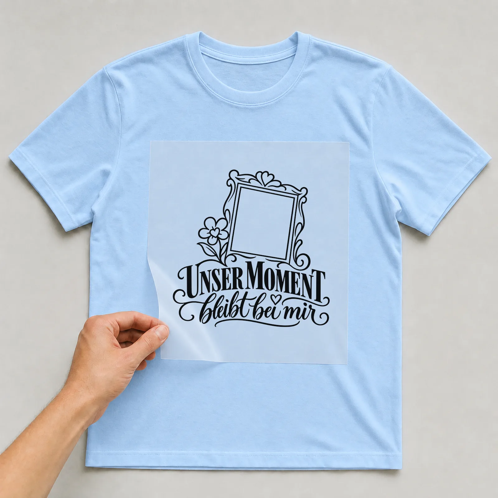 Bügelbild „Unser Moment bleibt bei mir“ auf hellblauem T-Shirt, Folie wird aufgelegt