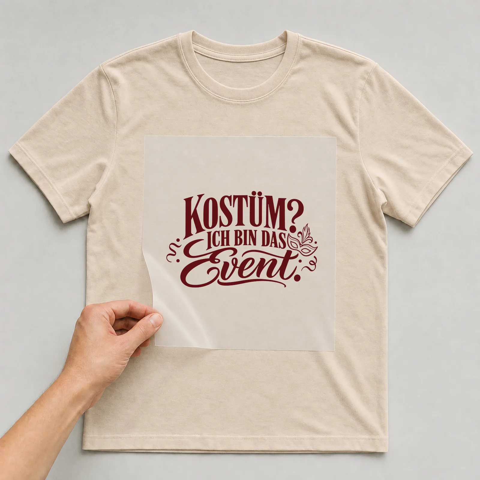 Bügelbild „Kostüm? Ich bin das Event.“ auf beigem T-Shirt, Folie wird aufgelegt