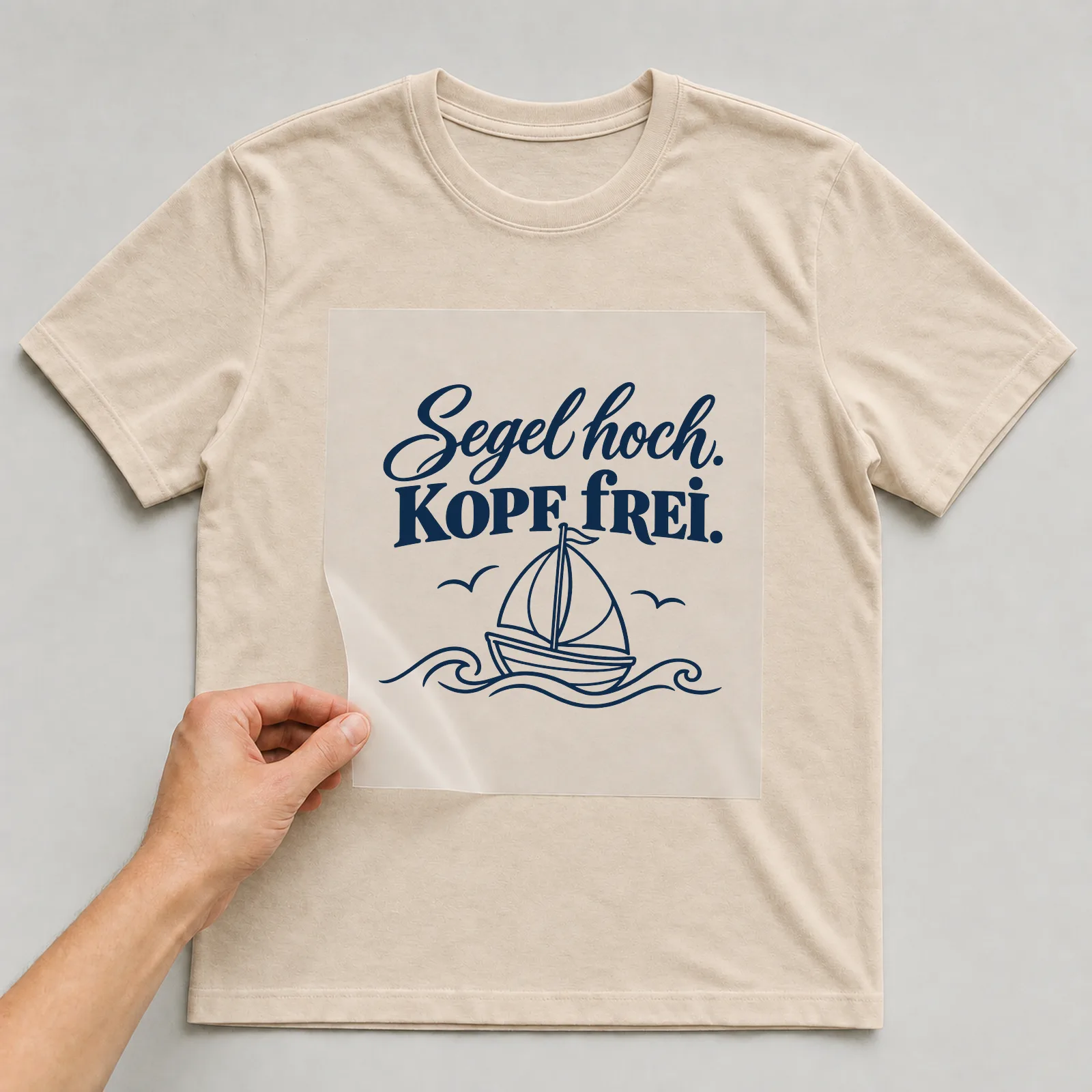 Bügelbild „Segel hoch. Kopf frei.“ auf beigem T-Shirt, Folie wird aufgelegt