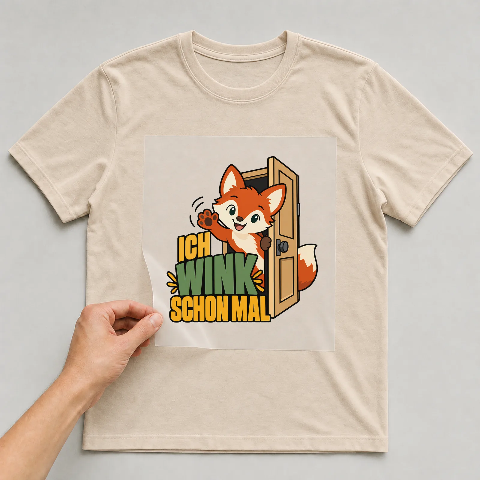 Bügelbild „Ich wink schon mal“ auf beigem T-Shirt, Folie wird aufgelegt