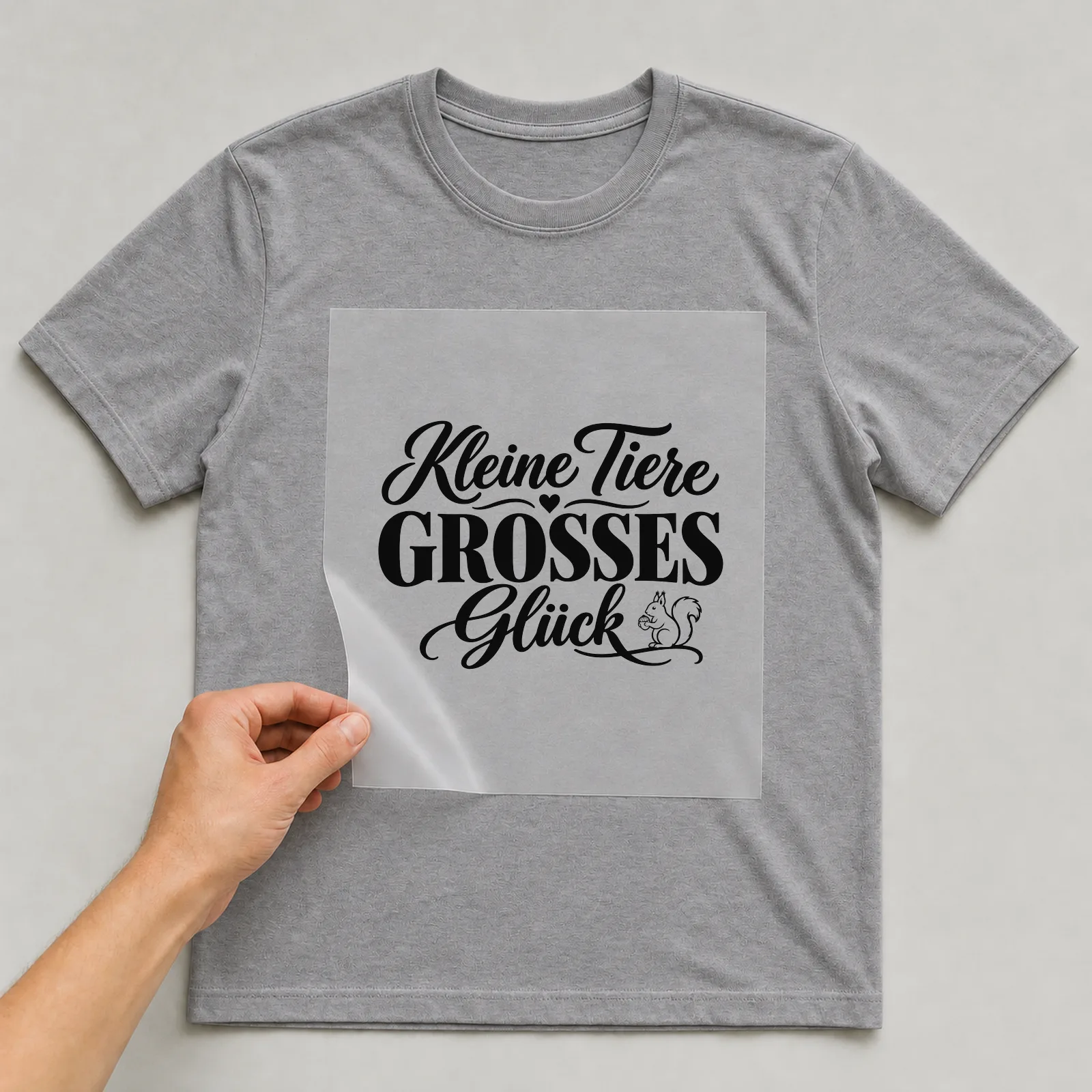 Bügelbild „Kleine Tiere großes Glück“ auf grauem T-Shirt, Folie wird aufgelegt