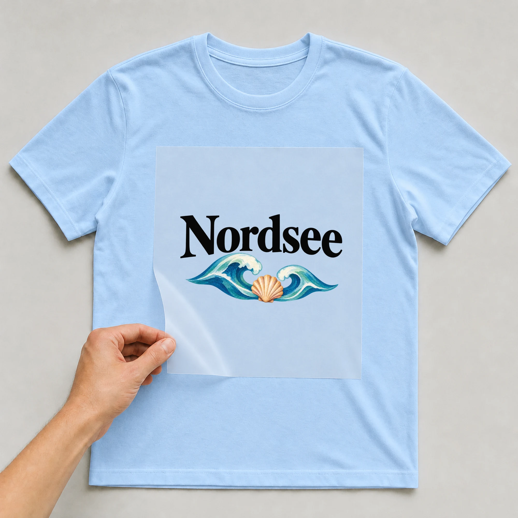Bügelbild „Nordsee“ auf babyblauem T-Shirt, Folie wird aufgelegt