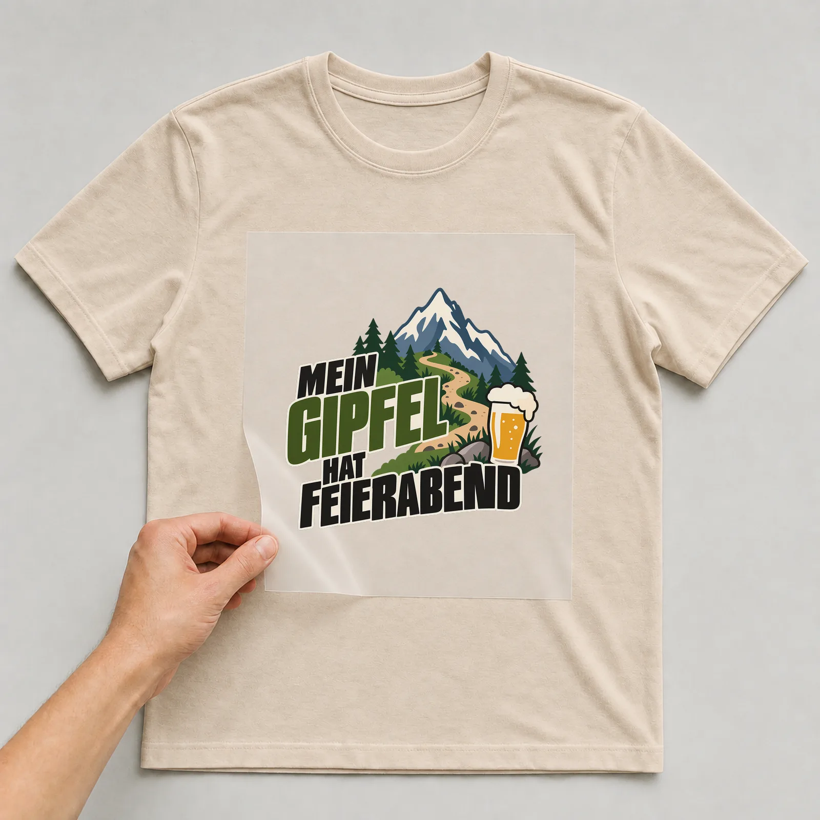 Bügelbild „Mein Gipfel hat Feierabend“ auf beigem T-Shirt, Folie wird aufgelegt