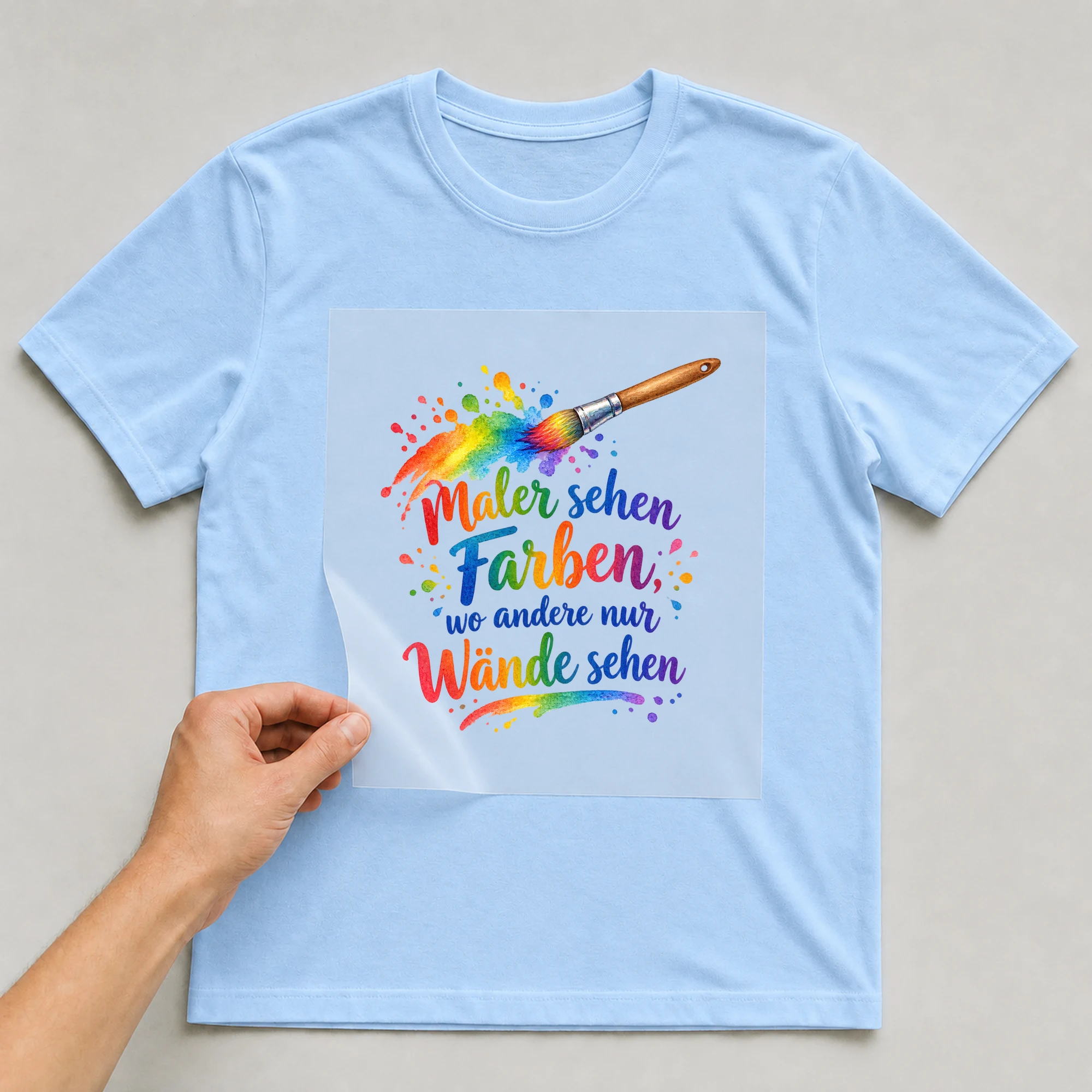 Bügelbild „Maler sehen Farben, wo andere nur Wände sehen“ auf babyblauem T-Shirt, Folie wird aufgelegt