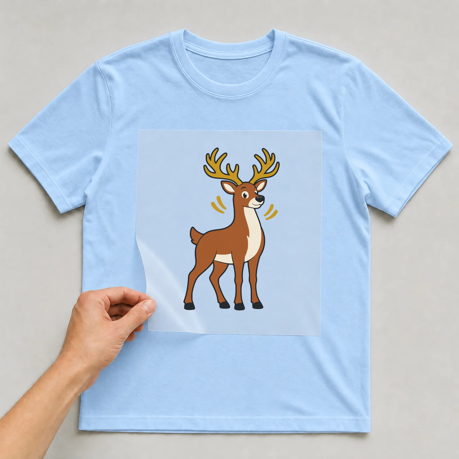 Bügelbild Hirsch im Comic-Stil auf hellblauem T-Shirt, Folie wird aufgelegt