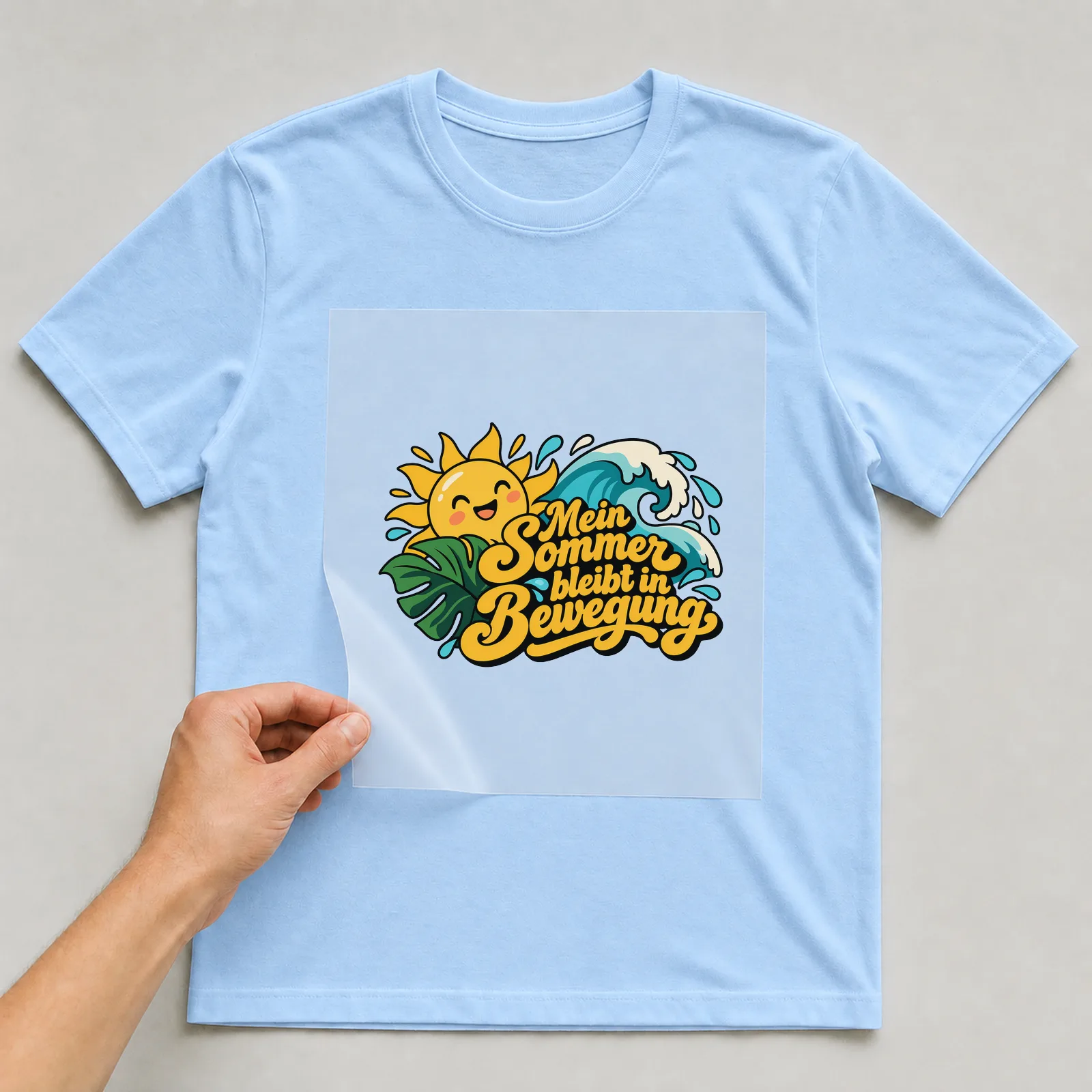 Bügelbild „Mein Sommer bleibt in Bewegung“ auf hellblauem T-Shirt, Folie wird aufgelegt
