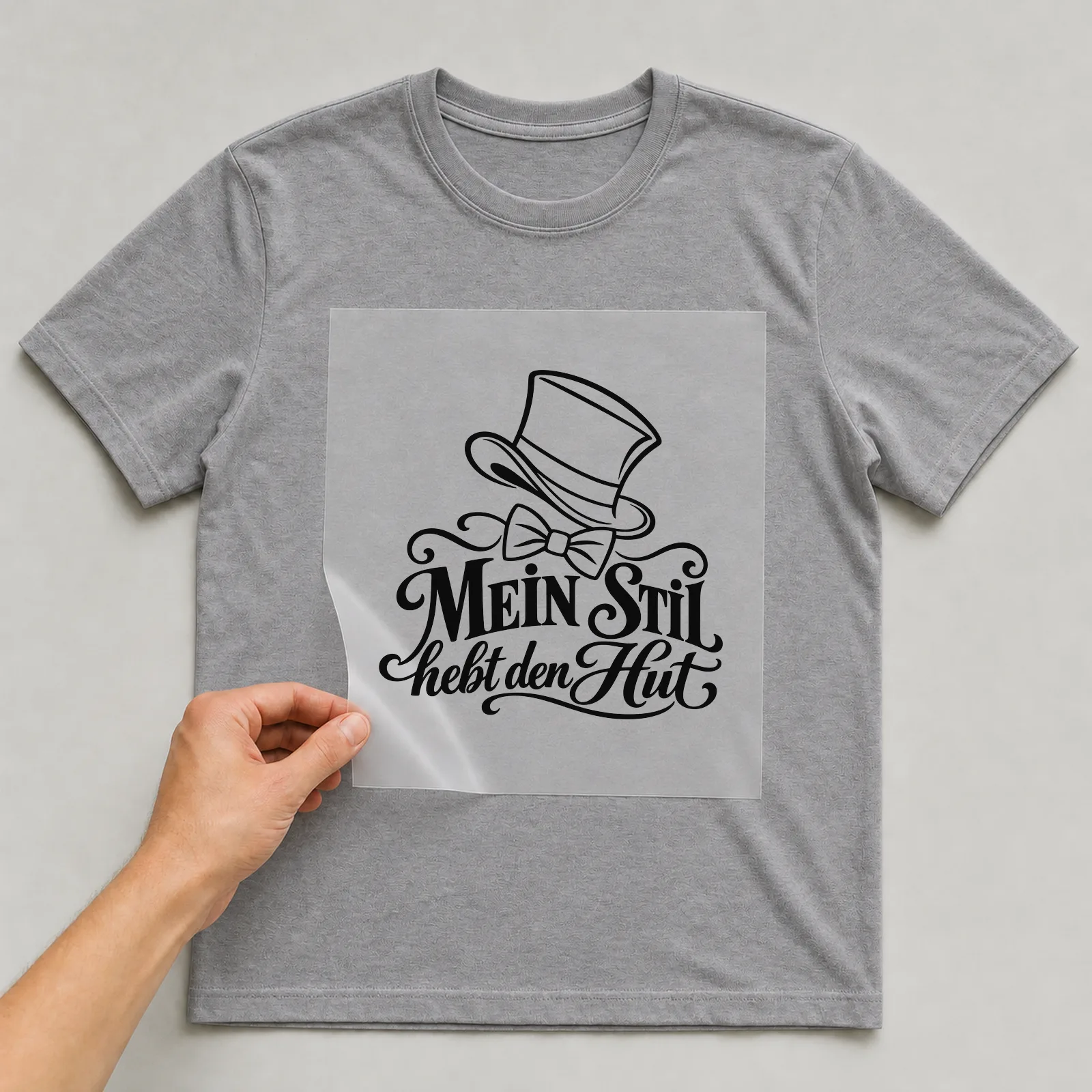 Bügelbild „Mein Stil hebt den Hut“ auf grauem T-Shirt, Folie wird aufgelegt