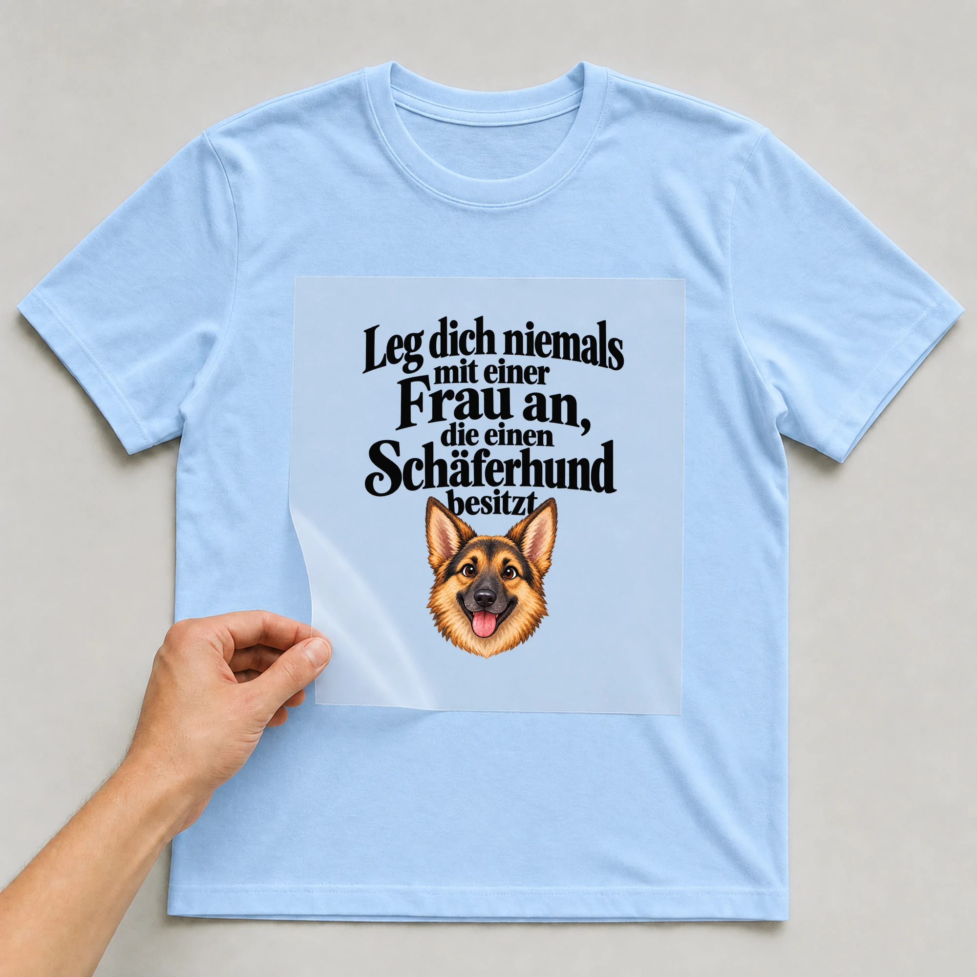 Bügelbild „Leg dich niemals mit einer Frau an, die einen Schäferhund besitzt“ auf babyblauem T-Shirt, Folie wird aufgelegt