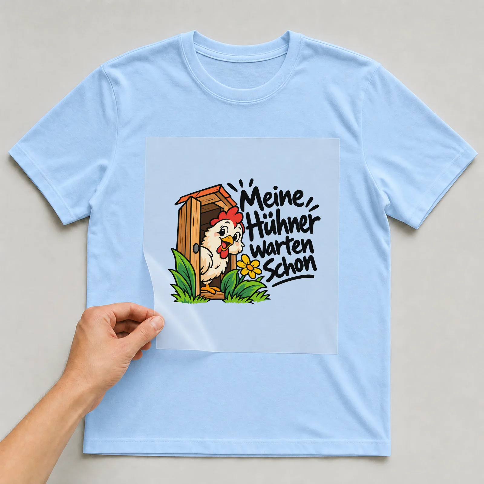 Bügelbild „Meine Hühner warten schon“ auf hellblauem T-Shirt, Folie wird aufgelegt