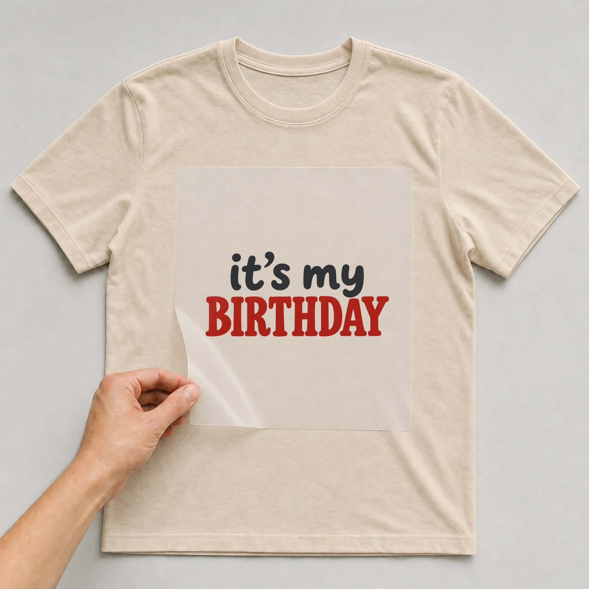 Bügelbild „it’s my BIRTHDAY“ auf beigem T-Shirt, Folie wird aufgelegt