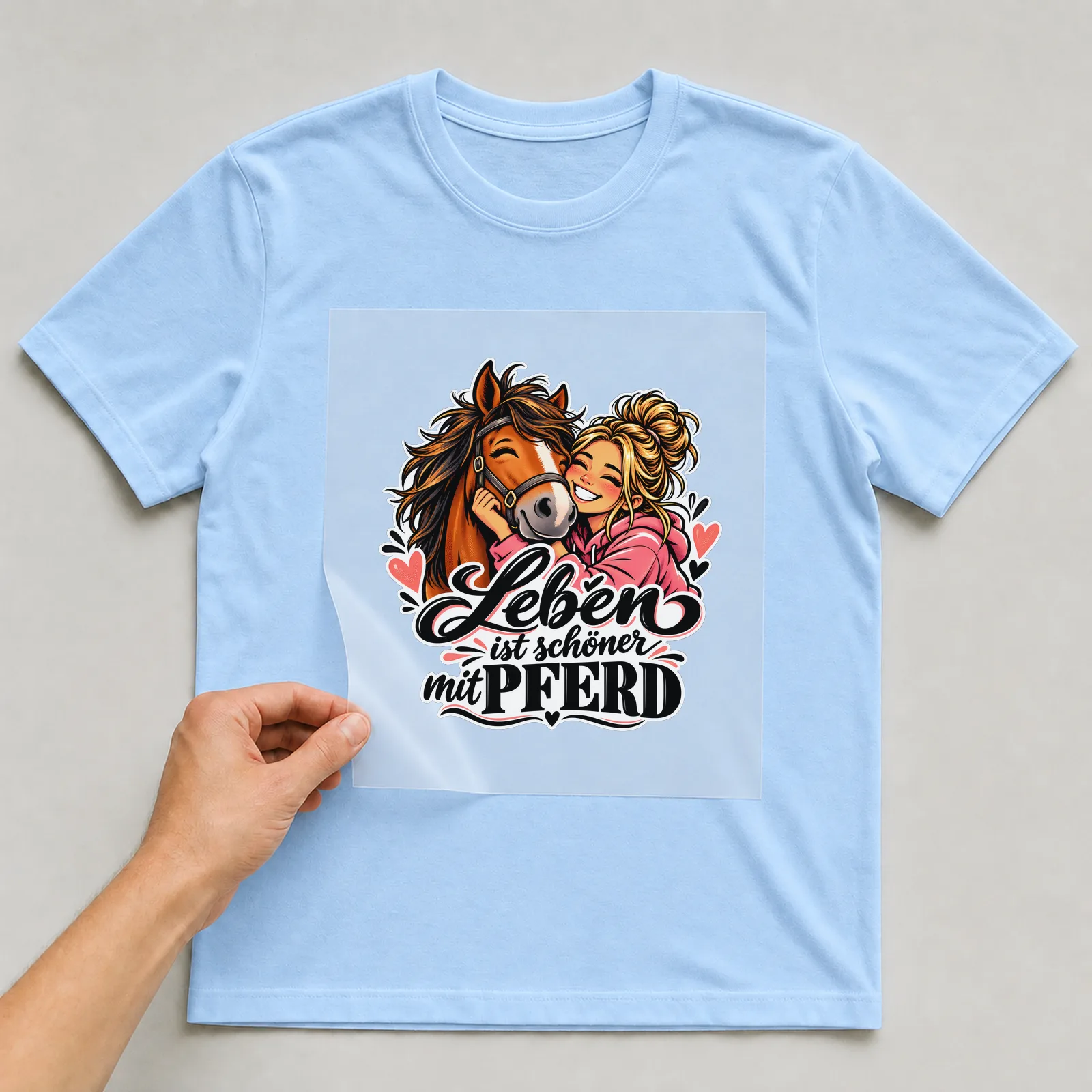 Bügelbild „Leben ist schöner mit Pferd“ auf hellblauem T-Shirt, Folie wird aufgelegt