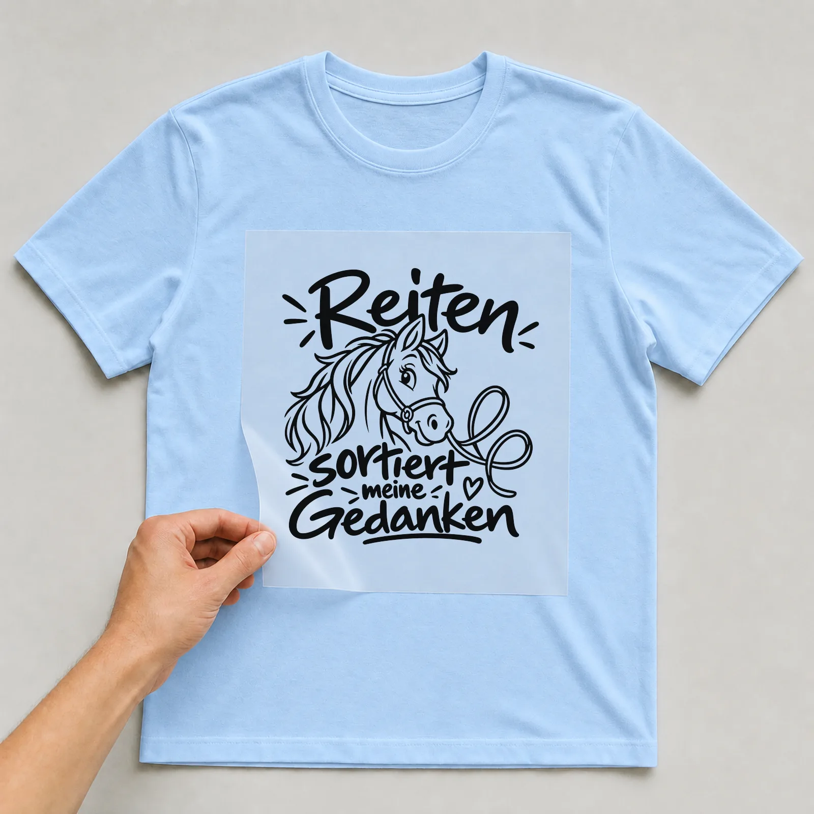 Bügelbild „Reiten sortiert meine Gedanken“ auf hellblauem T-Shirt, Folie wird aufgelegt