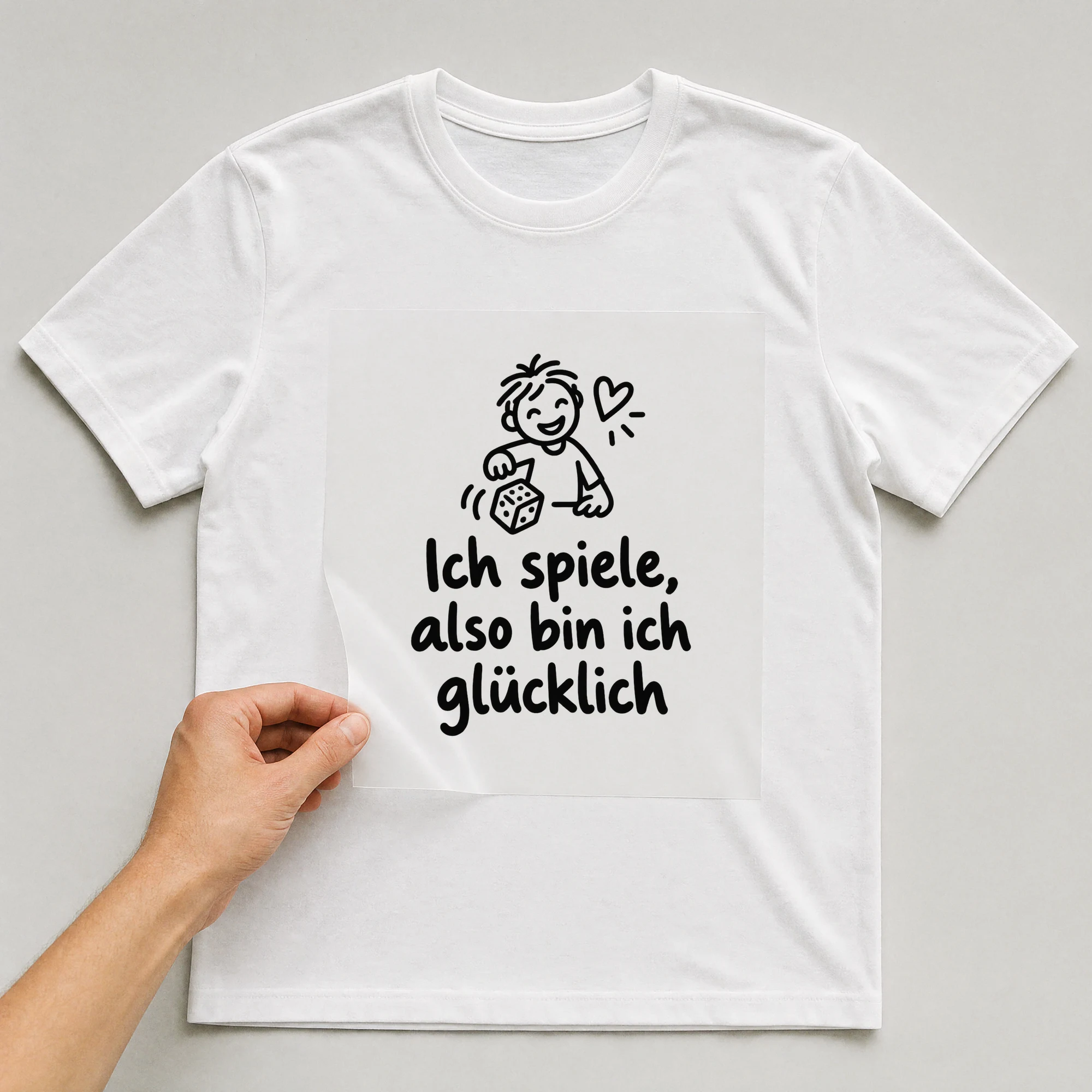 Bügelbild „Ich spiele, also bin ich glücklich“ auf weißem T-Shirt, Folie wird aufgelegt