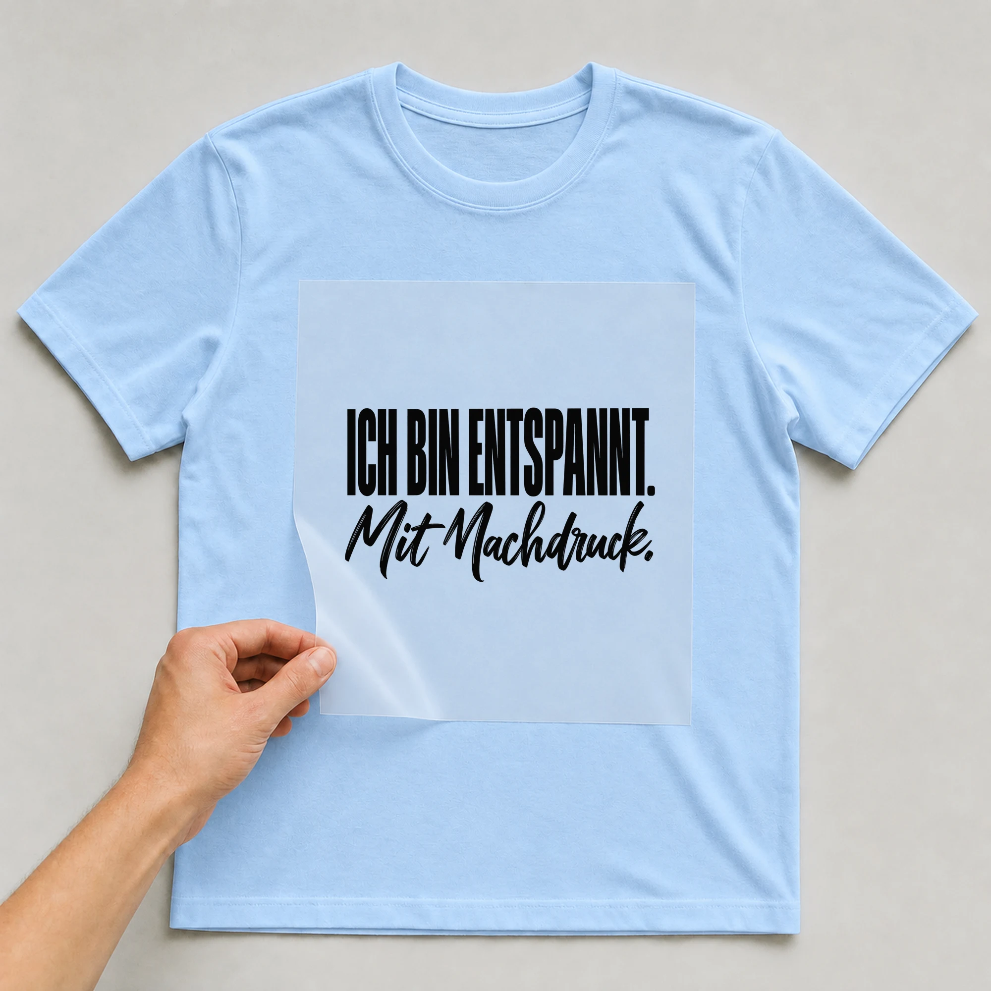 Bügelbild „Ich bin entspannt. Mit Nachdruck.“ auf babyblauem T-Shirt, Folie wird aufgelegt