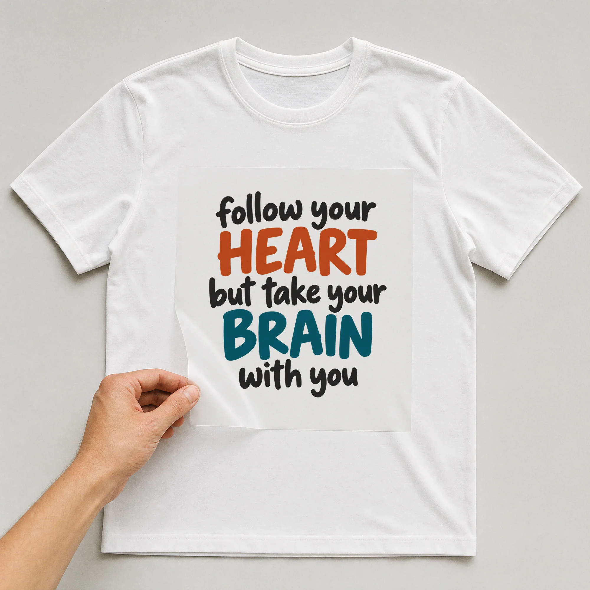 Bügelbild „Follow Your Heart But Take Your Brain With You“ auf weißem T-Shirt, Folie wird aufgelegt