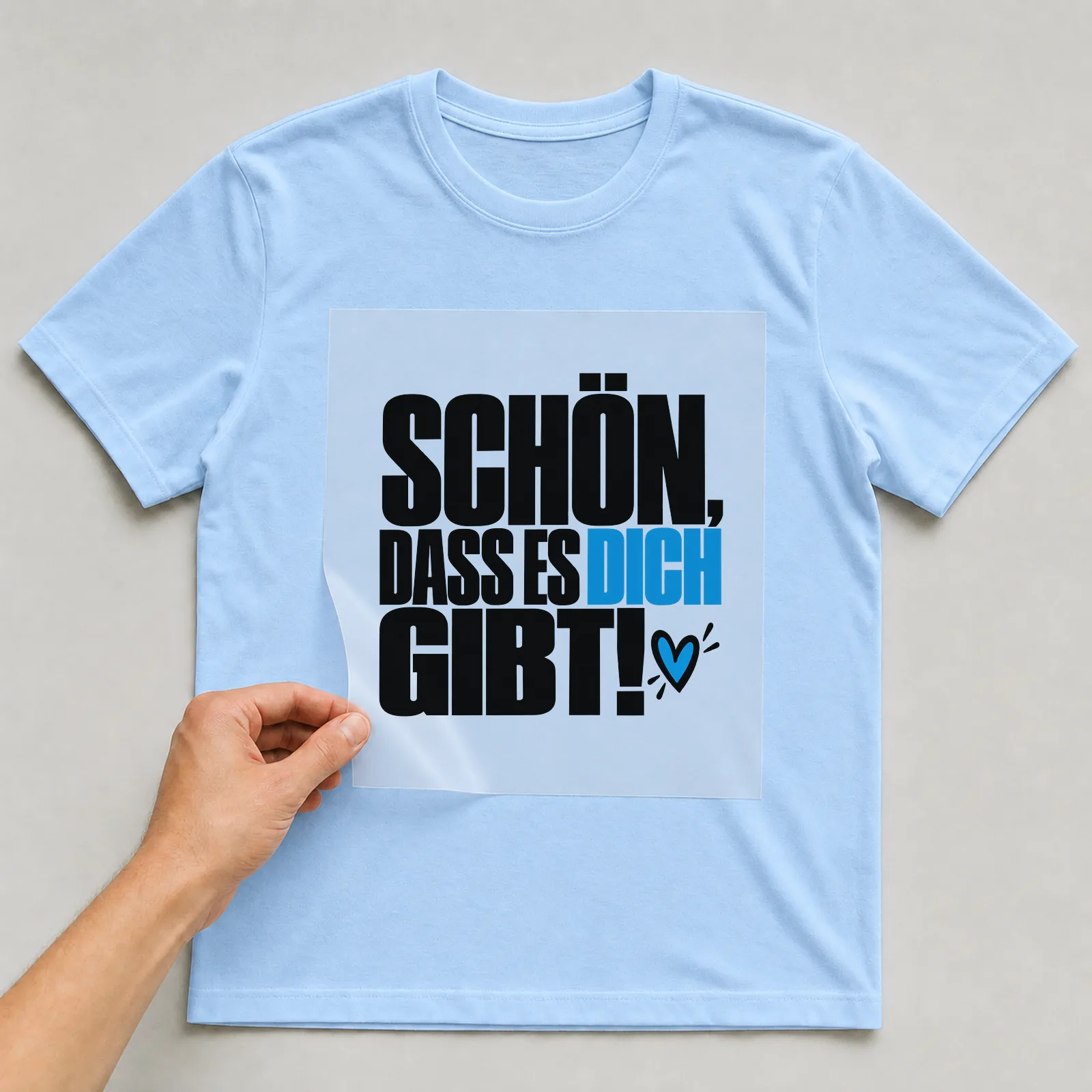 Bügelbild „Schön, dass es dich gibt!“ auf hellblauem T-Shirt, Folie wird aufgelegt