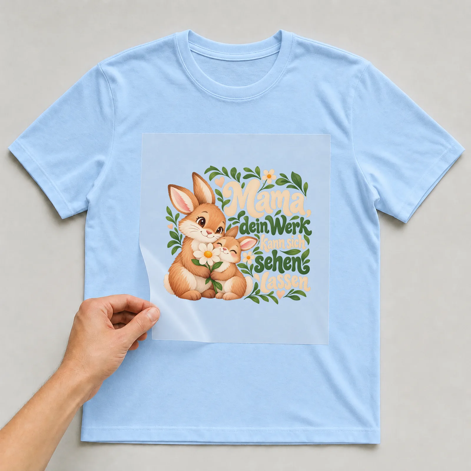 Bügelbild „Mama, dein Werk kann sich sehen lassen“ auf hellblauem T-Shirt, Folie wird aufgelegt