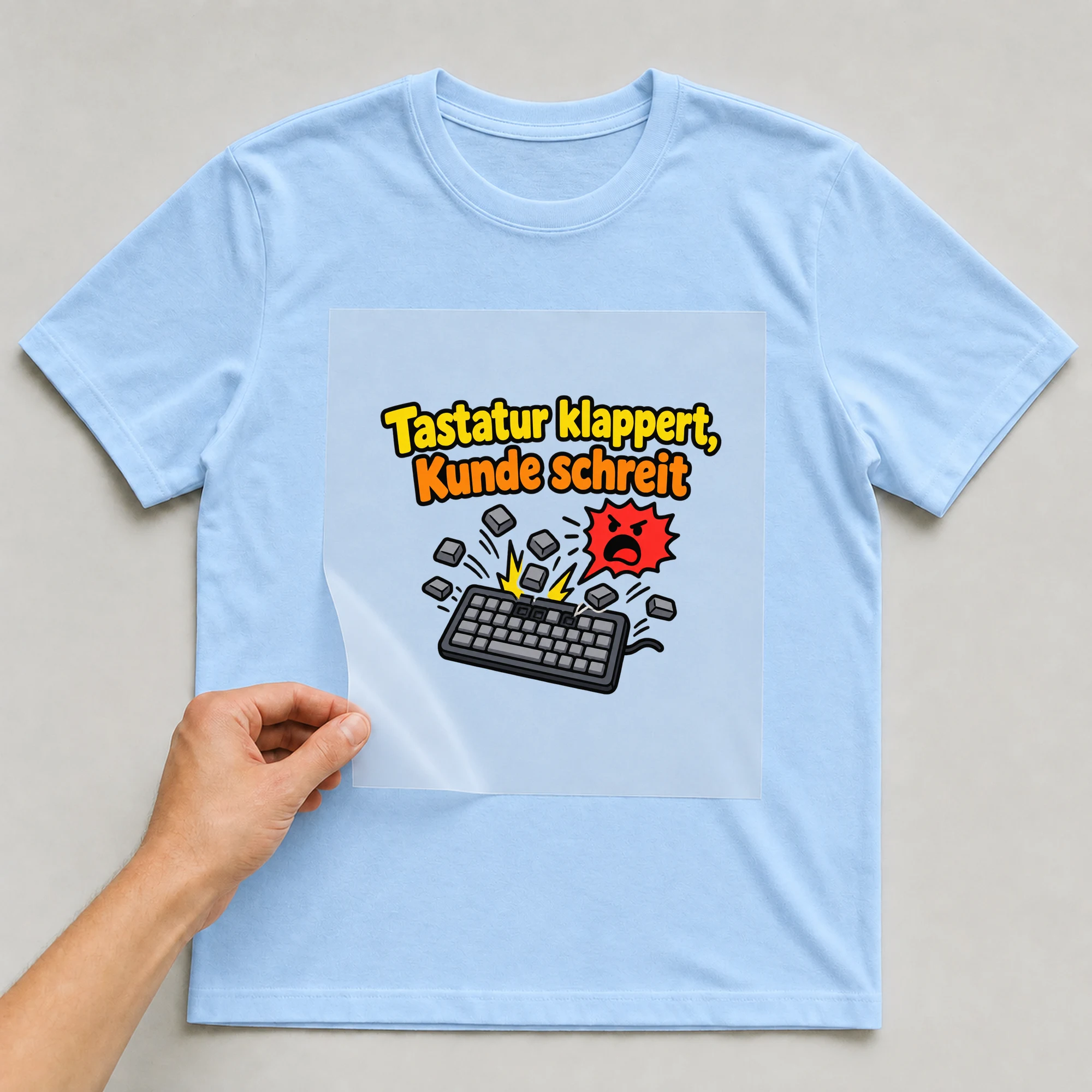 Bügelbild „Tastatur klappert, Kunde schreit“ auf babyblauem T-Shirt, Folie wird aufgelegt