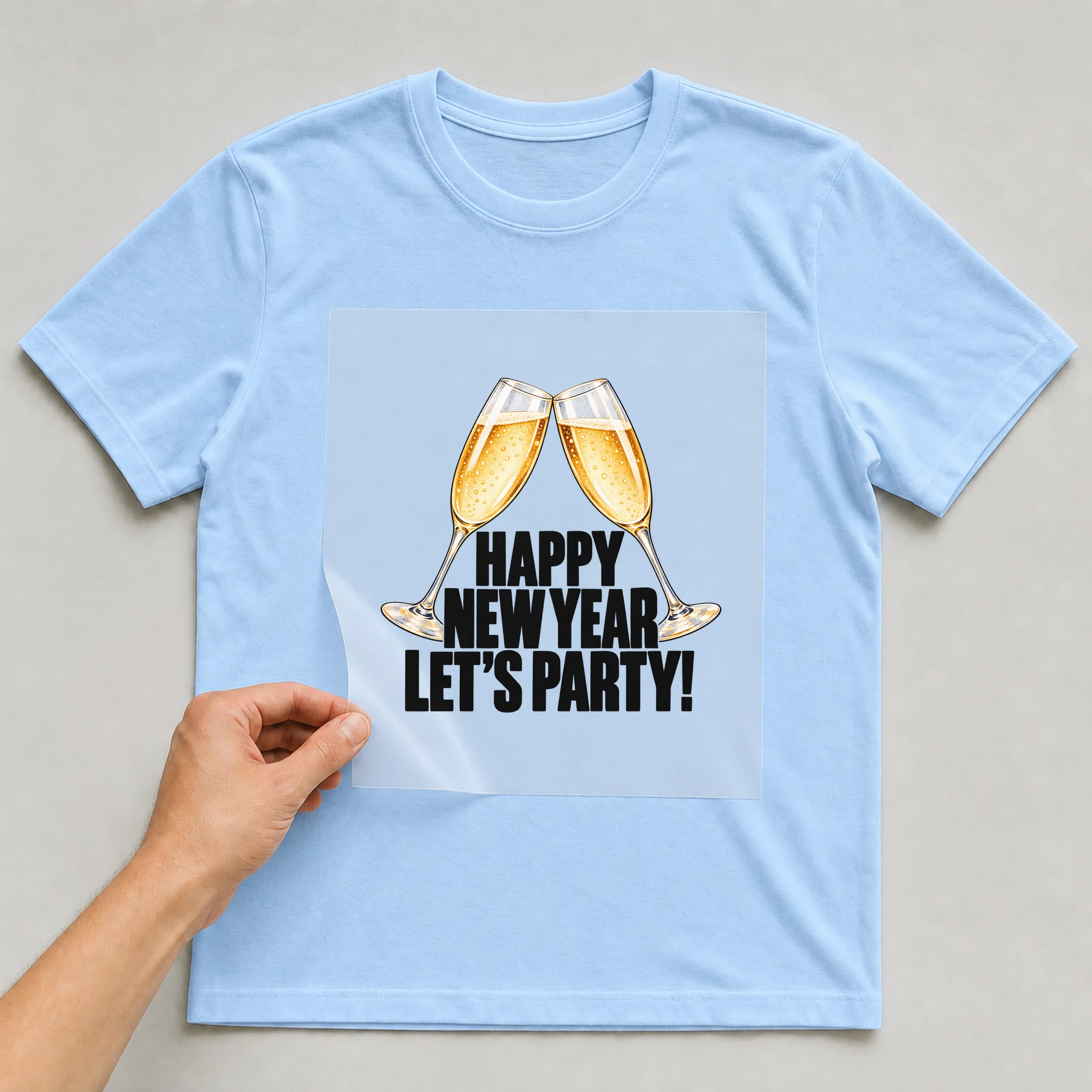 Bügelbild „Happy New Year Let's Party!“ auf babyblauem T-Shirt, Folie wird aufgelegt