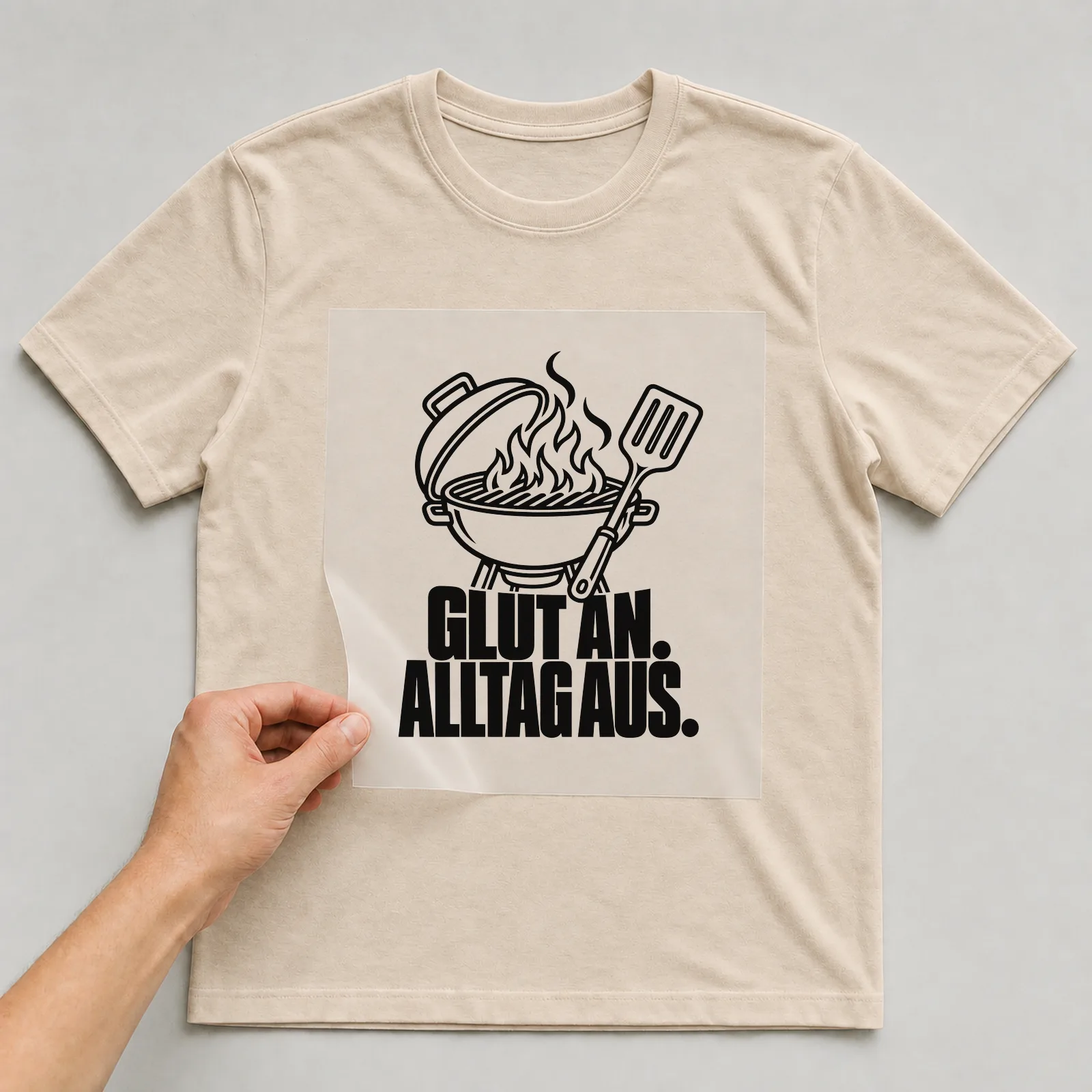 Bügelbild „Glut an. Alltag aus.“ auf beigem T-Shirt, Folie wird aufgelegt