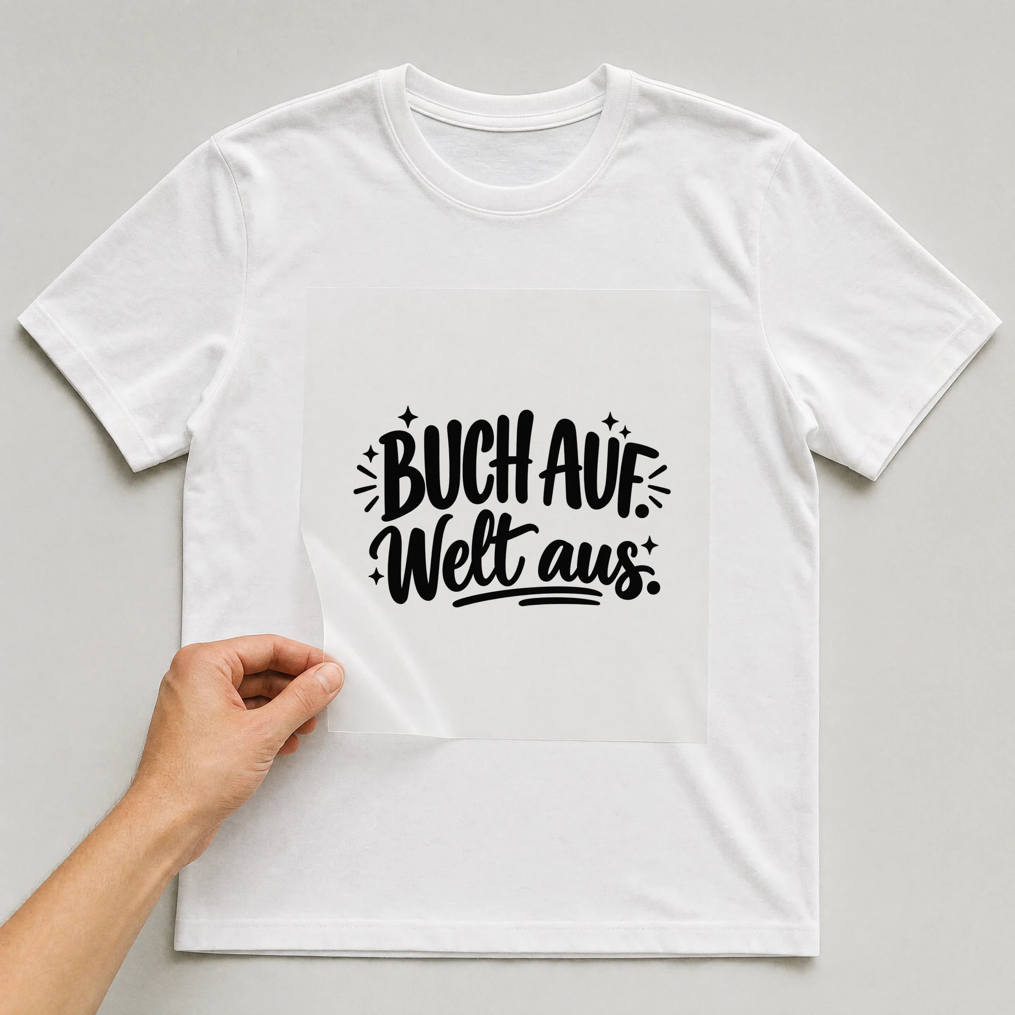 Bügelbild „Buch auf. Welt aus.“ auf weißem T-Shirt, Folie wird aufgelegt