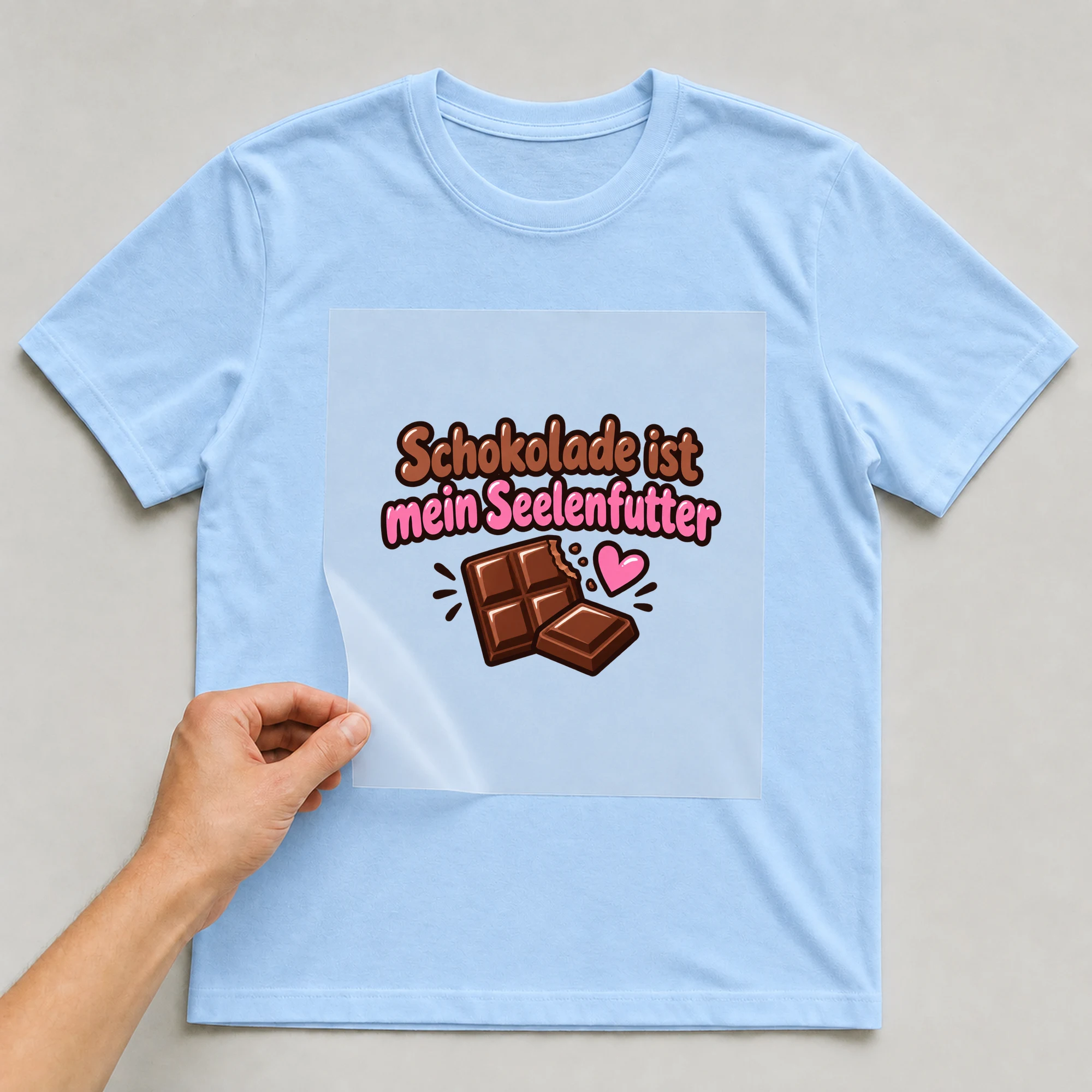 Bügelbild „Schokolade ist mein Seelenfutter“ auf babyblauem T-Shirt, Folie wird aufgelegt