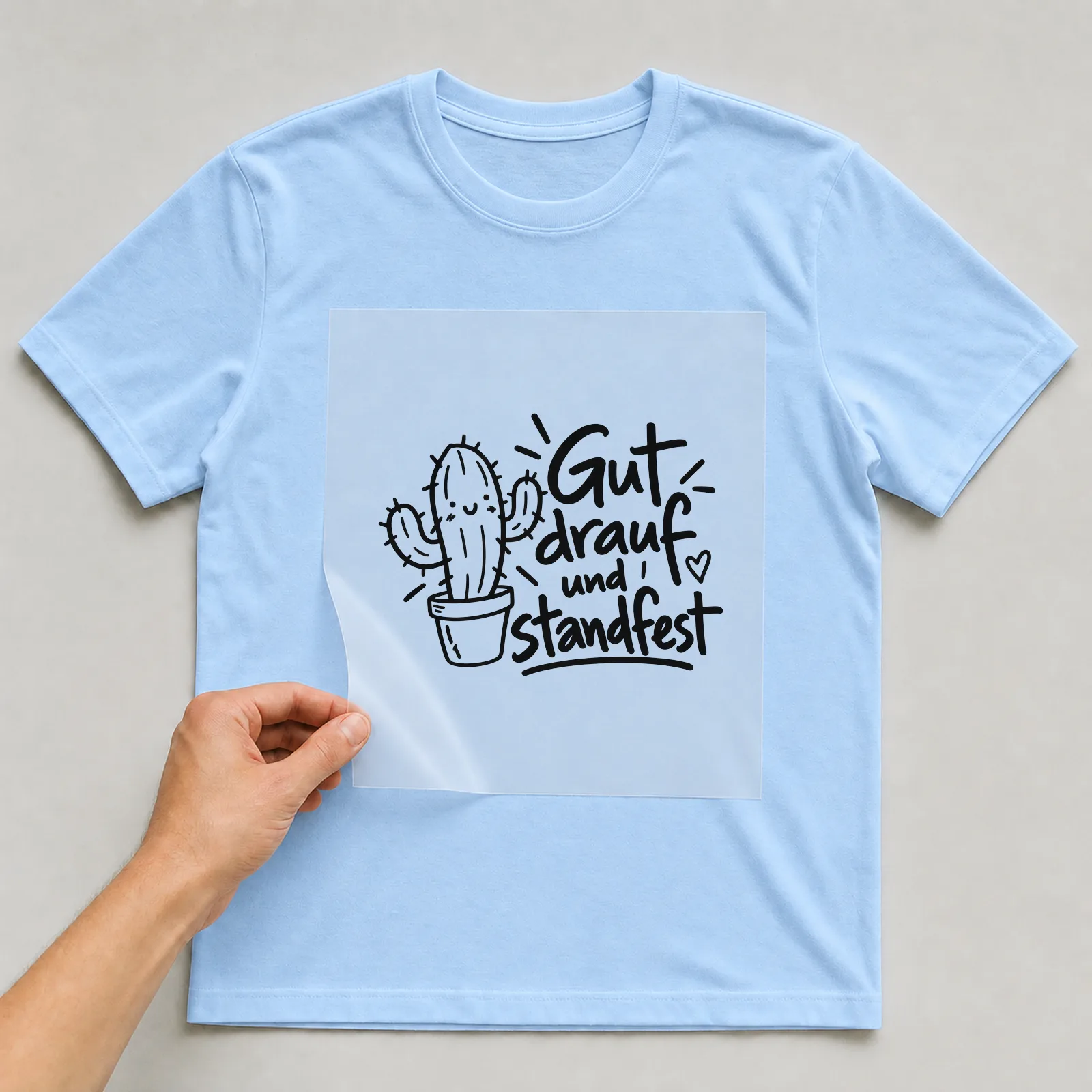 Bügelbild „Gut drauf und standfest“ auf hellblauem T-Shirt, Folie wird aufgelegt