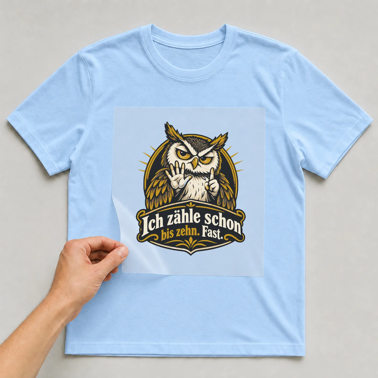 Bügelbild Ich zähle schon bis zehn. Fast. auf hellblauem T-Shirt, Folie wird aufgelegt