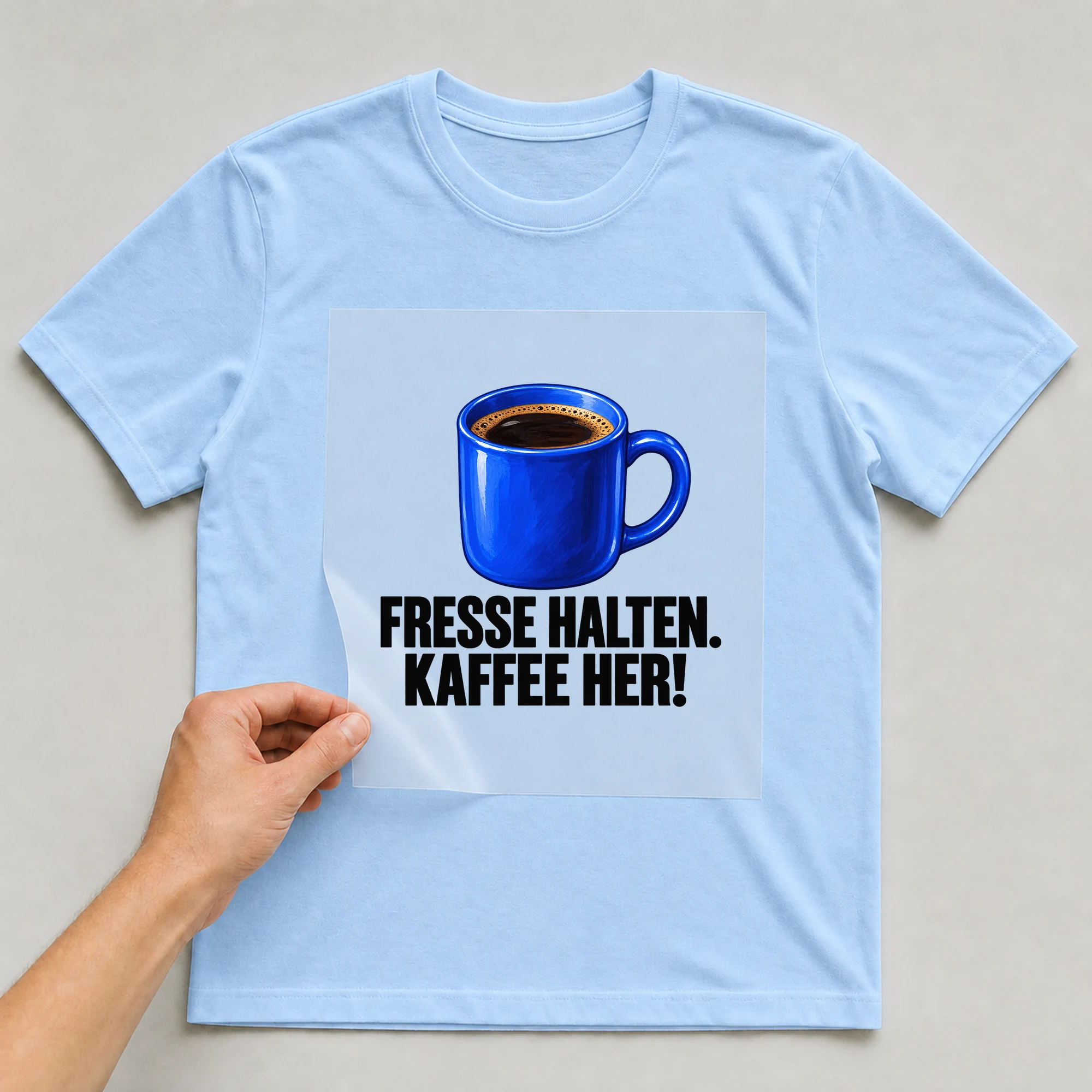 Bügelbild „Fr**se HALTEN. KAFFEE HER!“ auf babyblauem T-Shirt, Folie wird aufgelegt