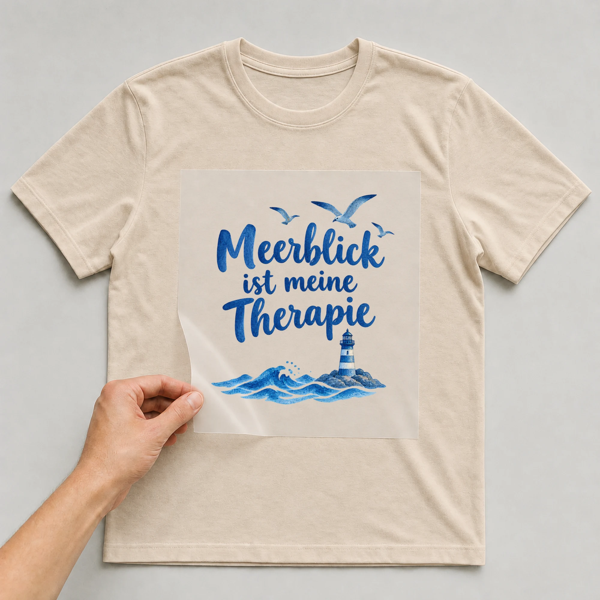 Bügelbild „Meerblick ist meine Therapie“ auf beigem T-Shirt, Folie wird aufgelegt