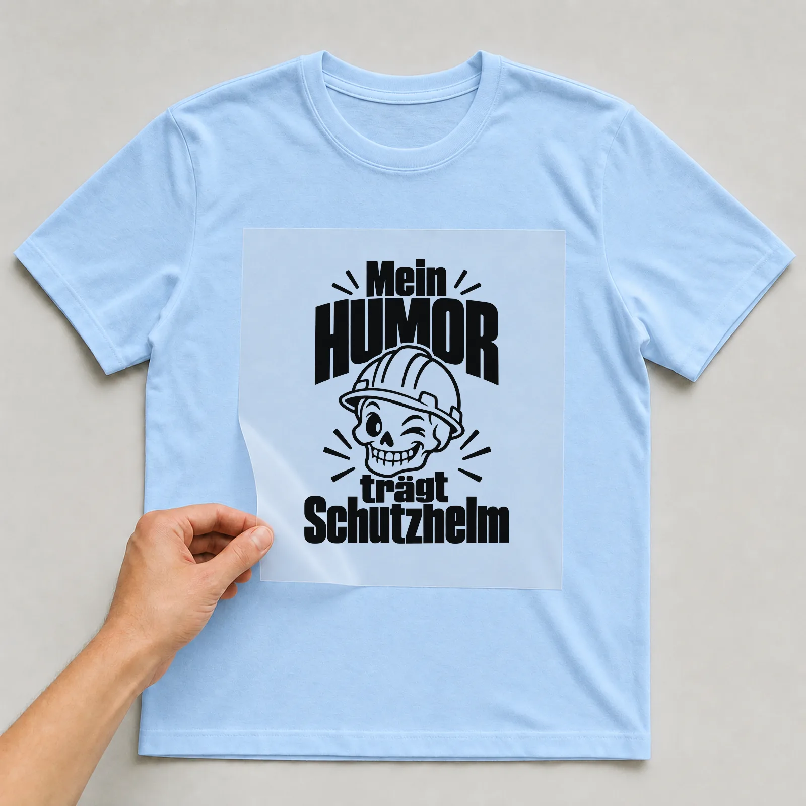 Bügelbild „Mein Humor trägt Schutzhelm“ auf hellblauem T-Shirt, Folie wird aufgelegt
