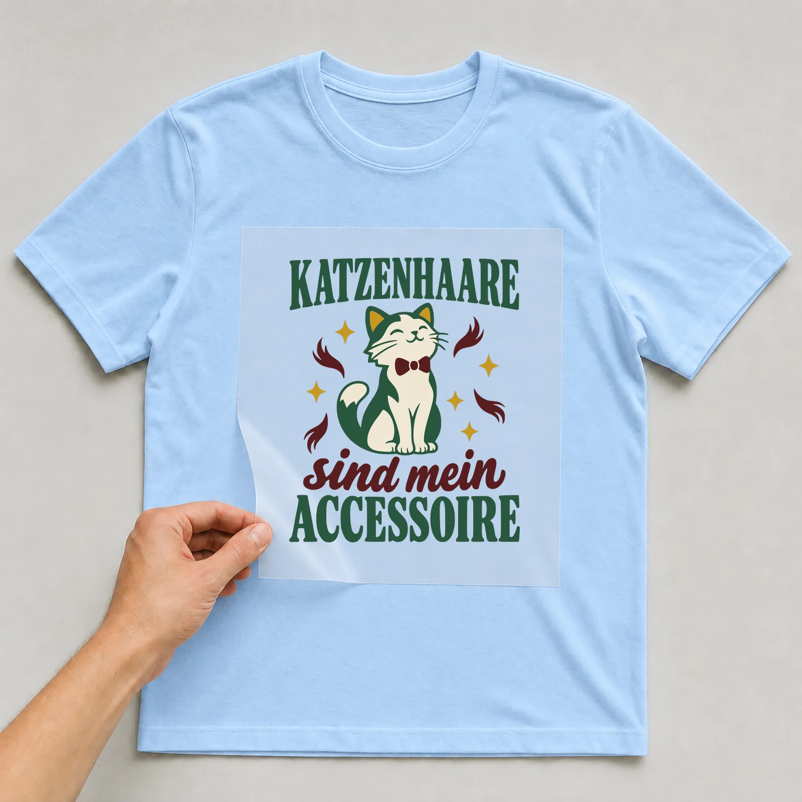 Bügelbild Katzenhaare sind mein Accessoire auf hellblauem T-Shirt, Folie wird aufgelegt