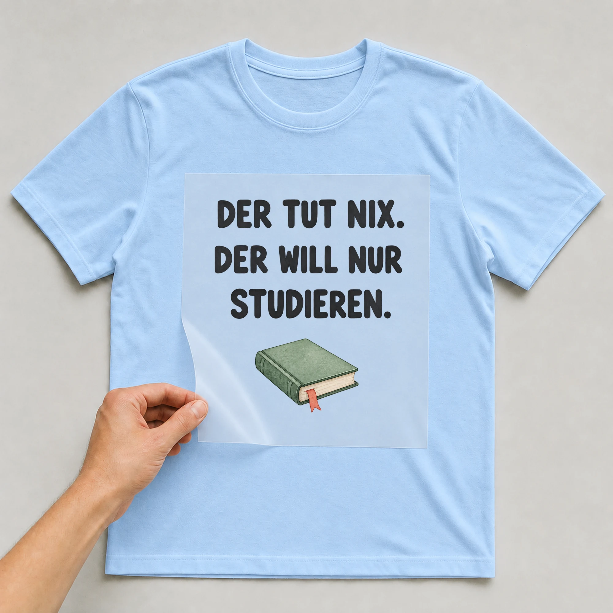 Bügelbild „DER TUT NIX. DER WILL NUR STUDIEREN.“ auf babyblauem T-Shirt, Folie wird aufgelegt
