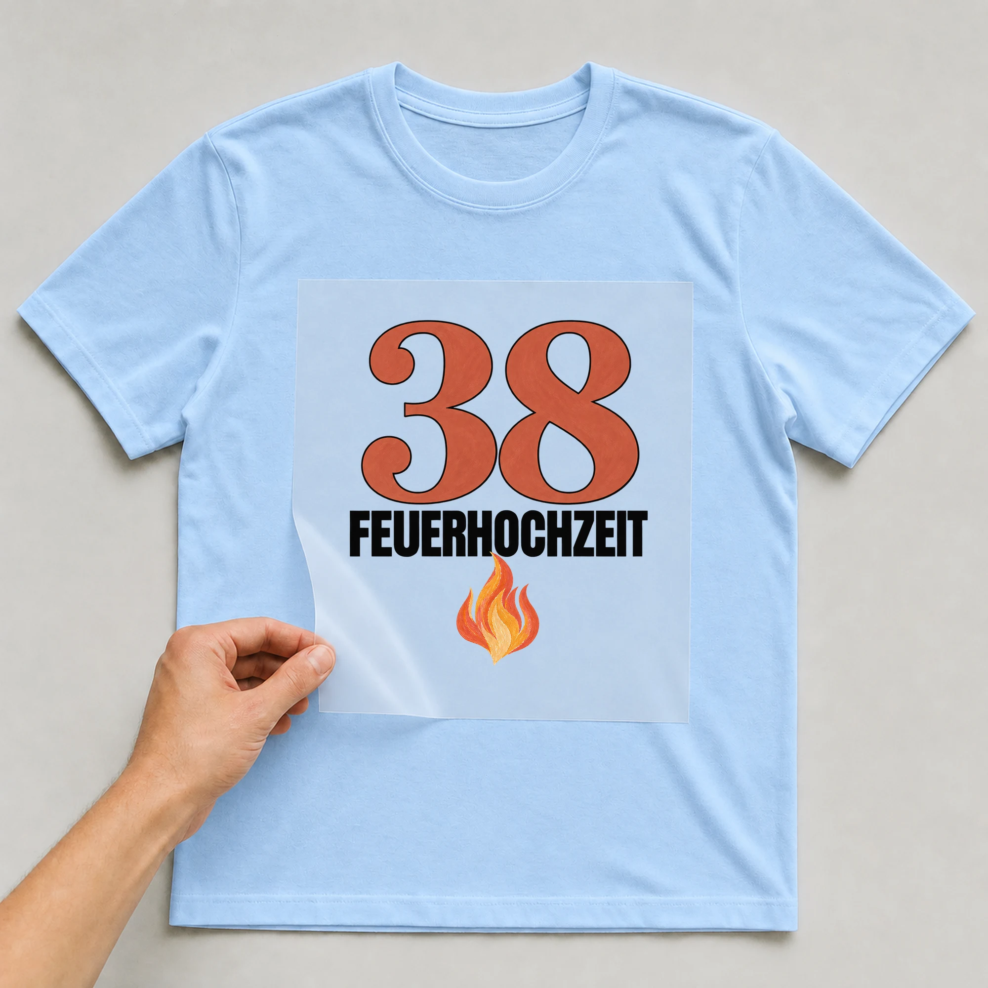 Bügelbild „38 Feuerhochzeit“ auf babyblauem T-Shirt, Folie wird aufgelegt