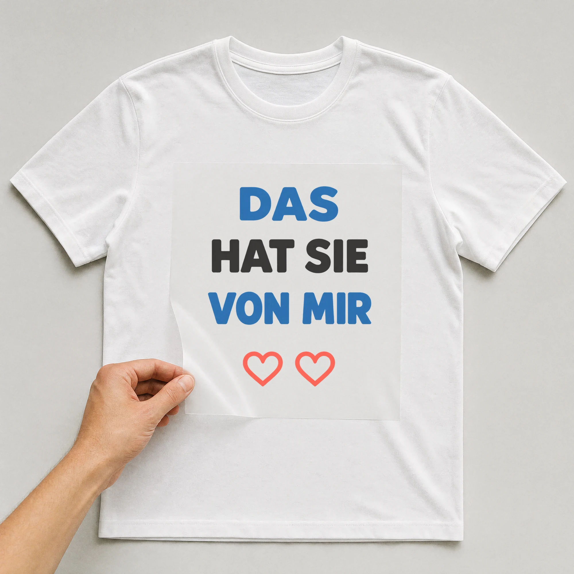 Bügelbild „DAS HAT SIE VON MIR“ auf weißem T-Shirt, Folie wird aufgelegt