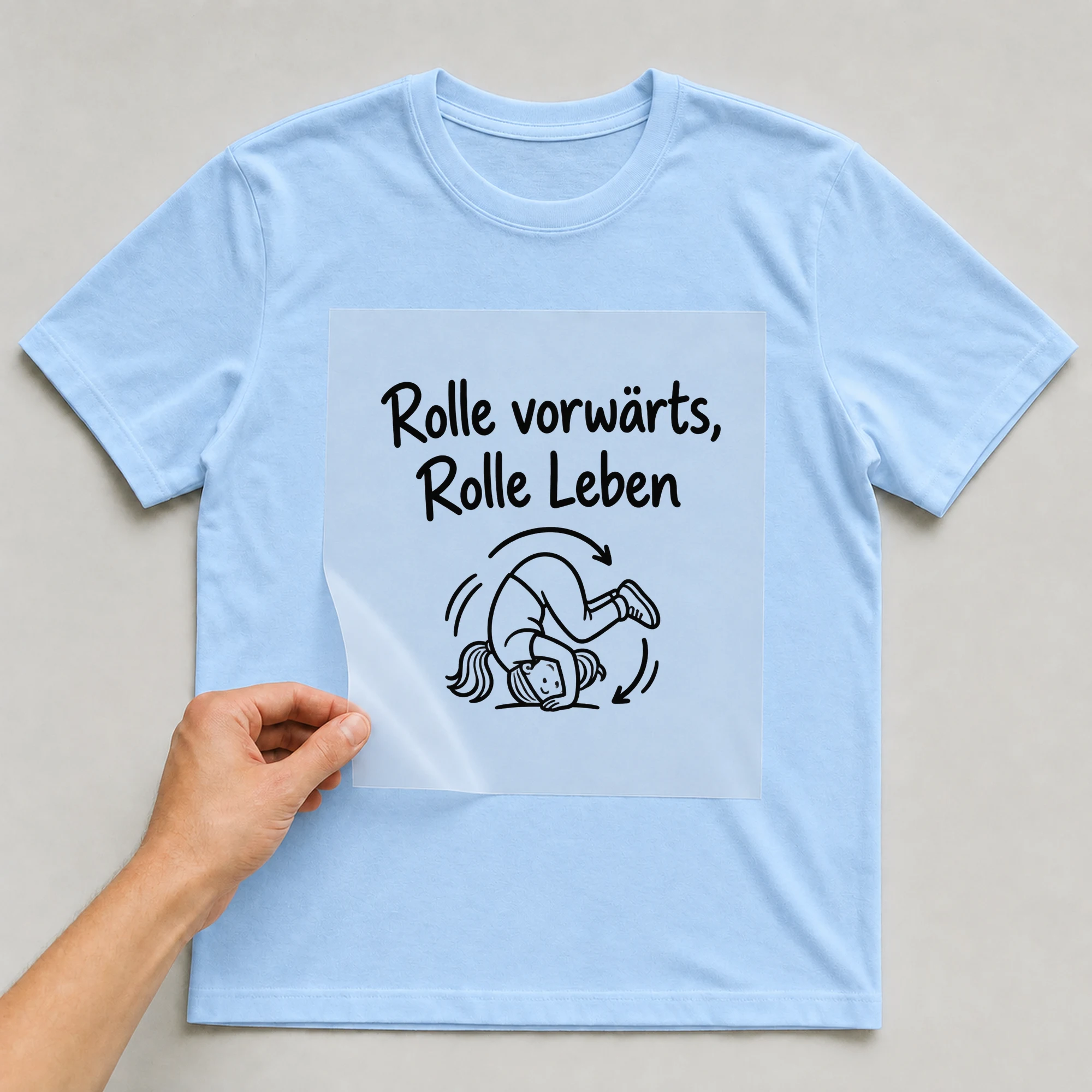 Bügelbild „Rolle vorwärts, Rolle Leben“ auf babyblauem T-Shirt, Folie wird aufgelegt