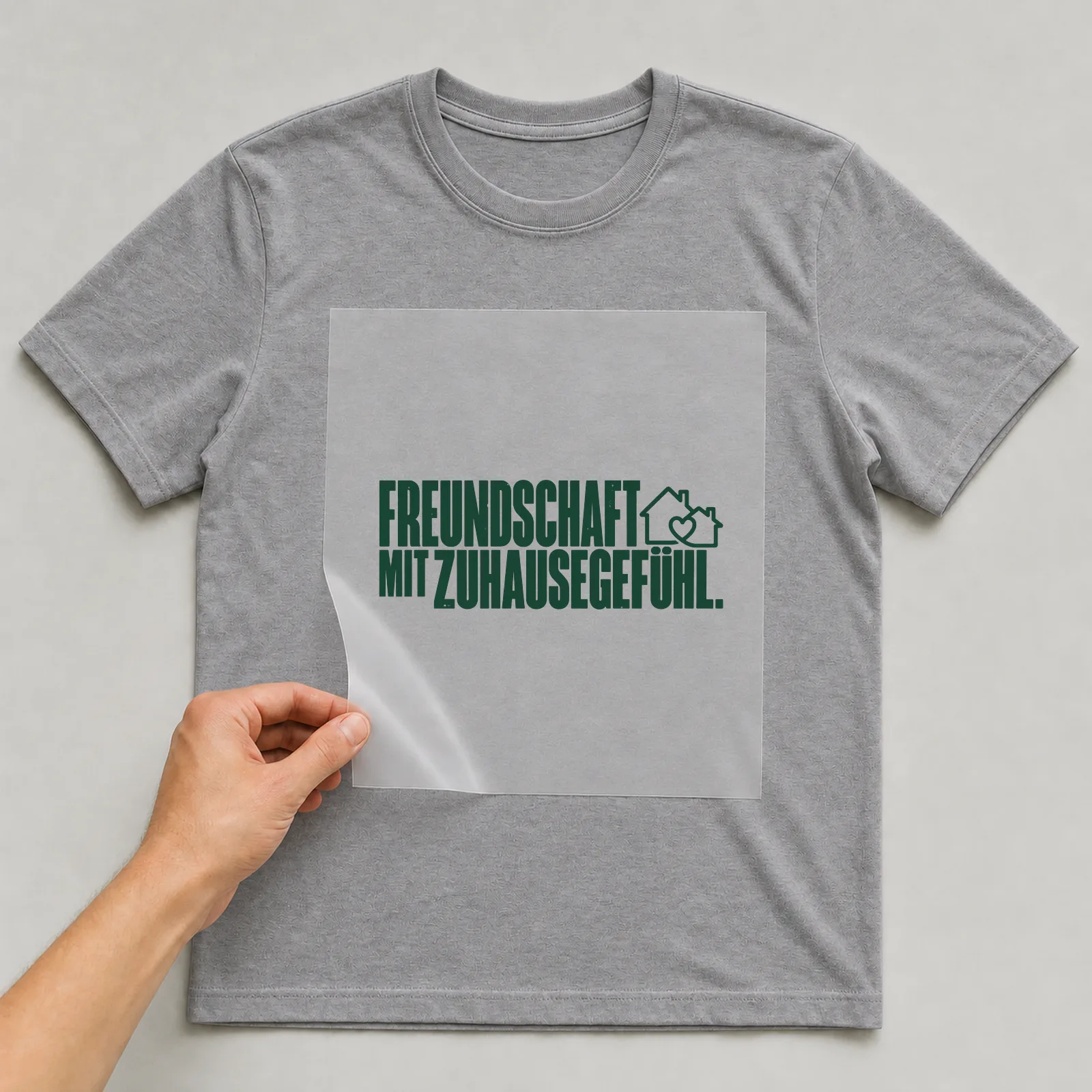 Bügelbild „Freundschaft mit Zuhausegefühl“ auf grauem T-Shirt, Folie wird aufgelegt