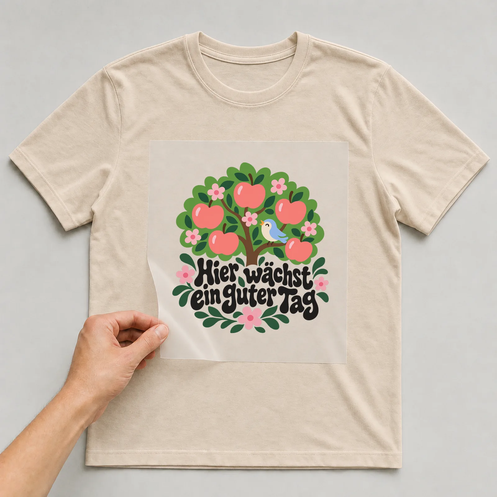 Bügelbild „Hier wächst ein guter Tag“ auf beigem T-Shirt, Folie wird aufgelegt