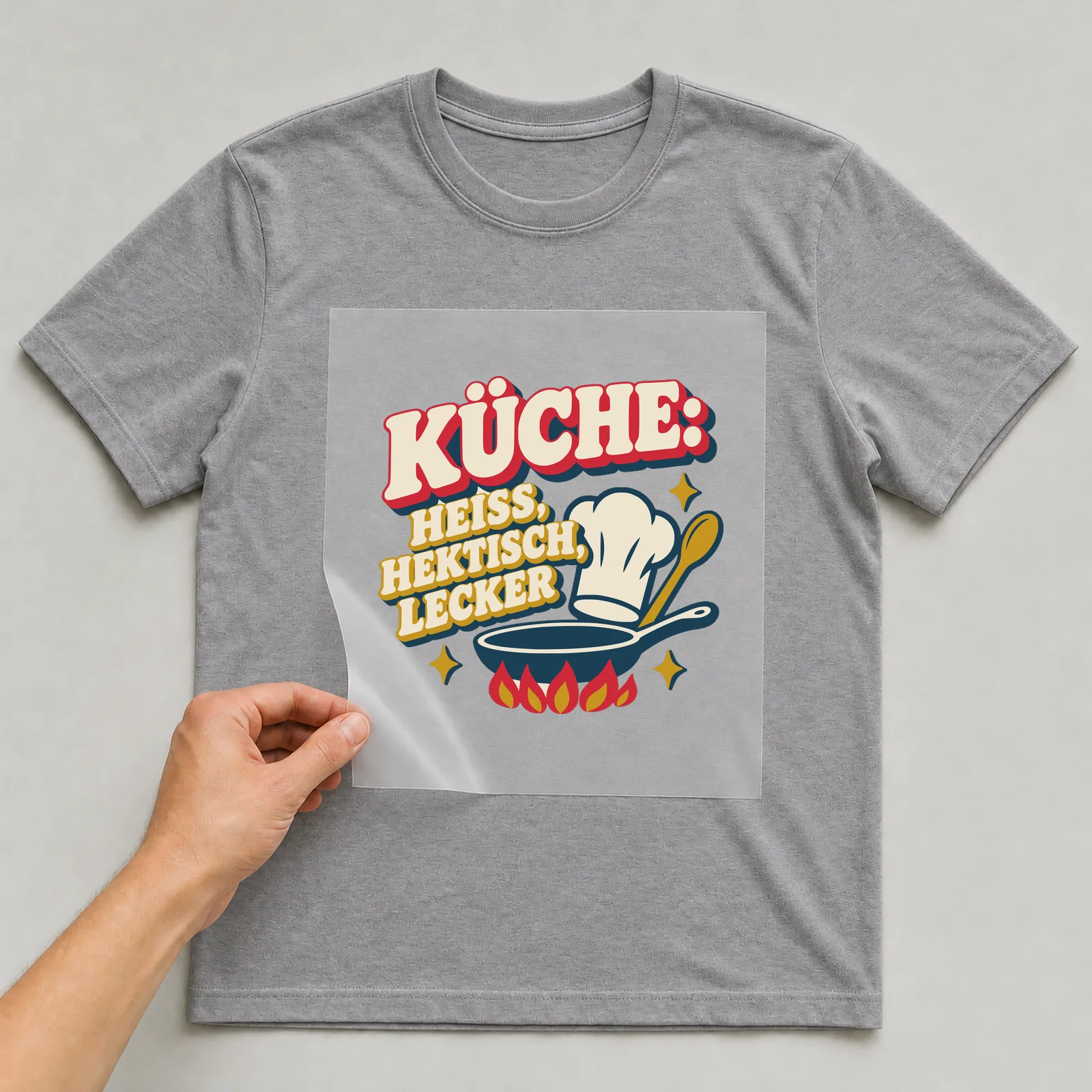 Bügelbild Küche: heiß, hektisch, lecker auf grauem T-Shirt, Folie wird aufgelegt