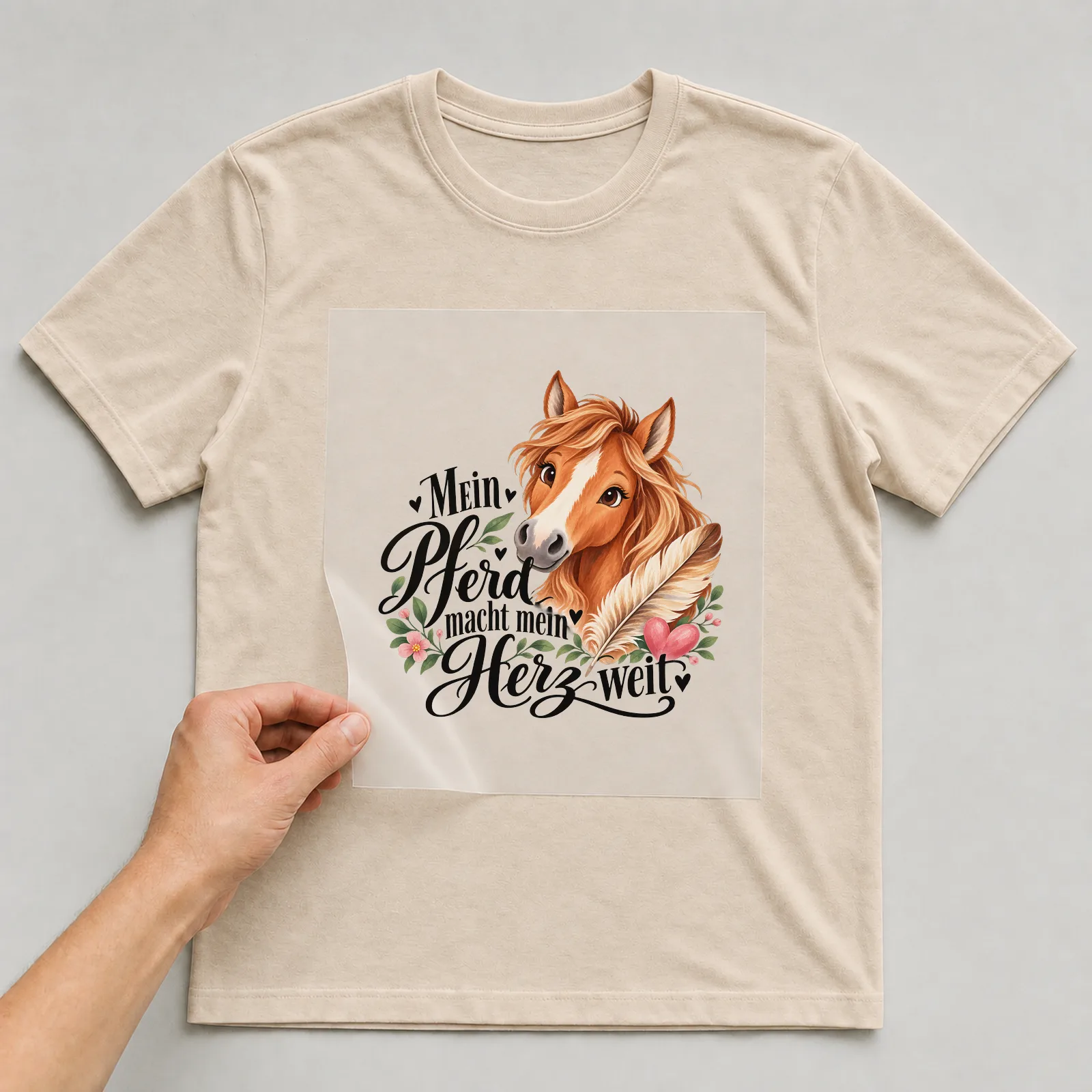 Bügelbild „Mein Pferd macht mein Herz weit“ auf beigem T-Shirt, Folie wird aufgelegt
