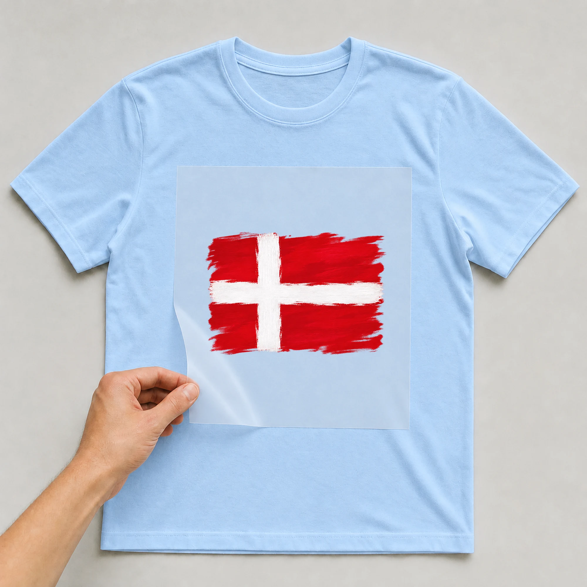 Bügelbild „Zerrissene Fahne Dänemark“ auf babyblauem T-Shirt, Folie wird aufgelegt
