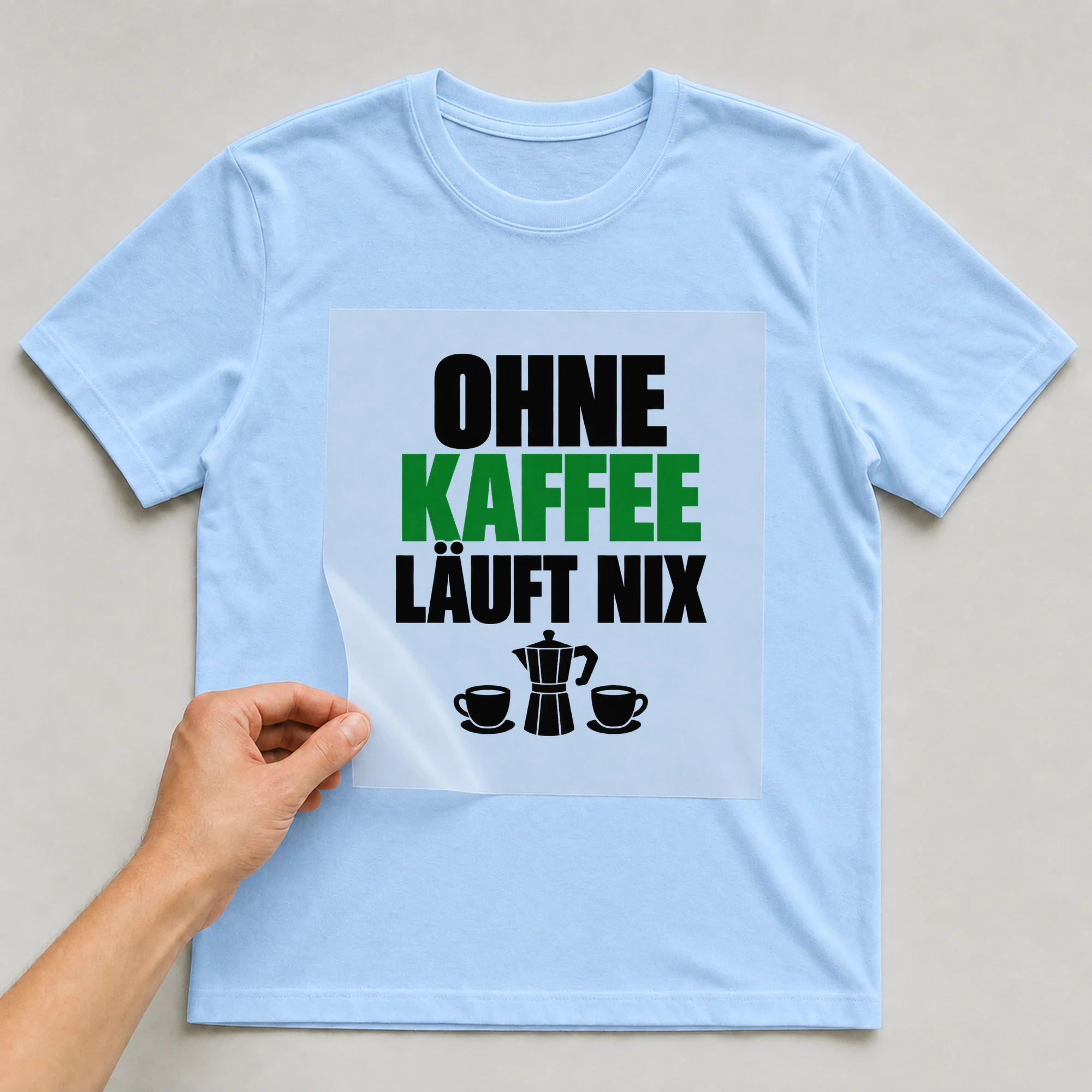 Bügelbild „Ohne Kaffee läuft nix“ auf hellblauem T-Shirt, Folie wird aufgelegt