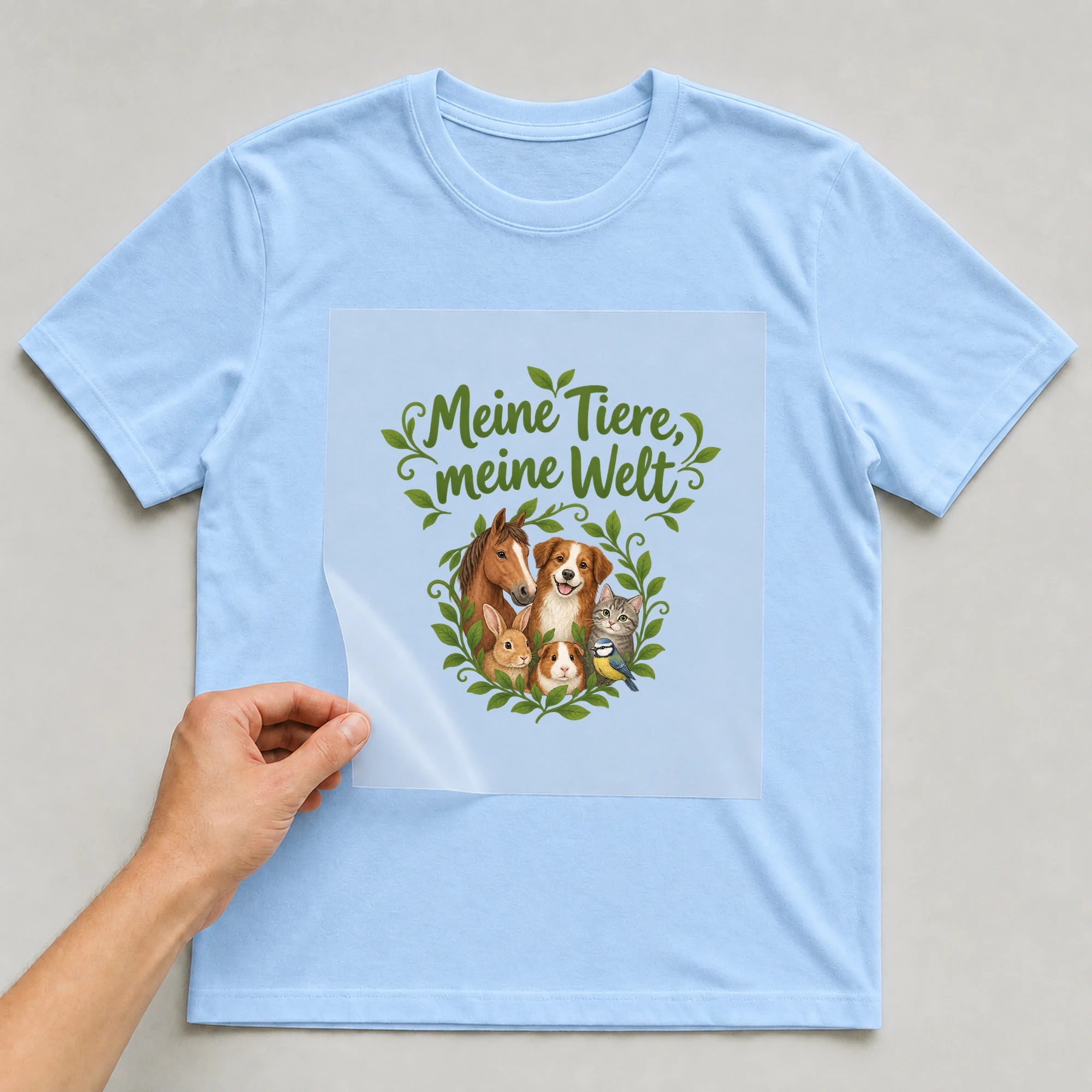 Bügelbild „Meine Tiere, meine Welt“ auf babyblauem T-Shirt, Folie wird aufgelegt