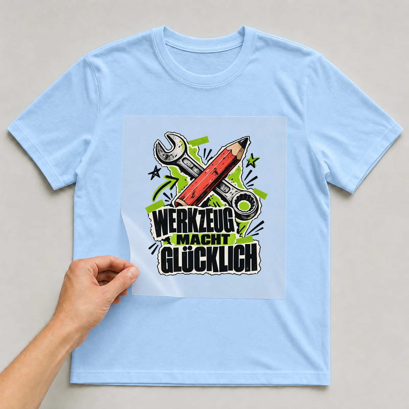 Bügelbild „Werkzeug macht glücklich“ auf hellblauem T-Shirt, Folie wird aufgelegt