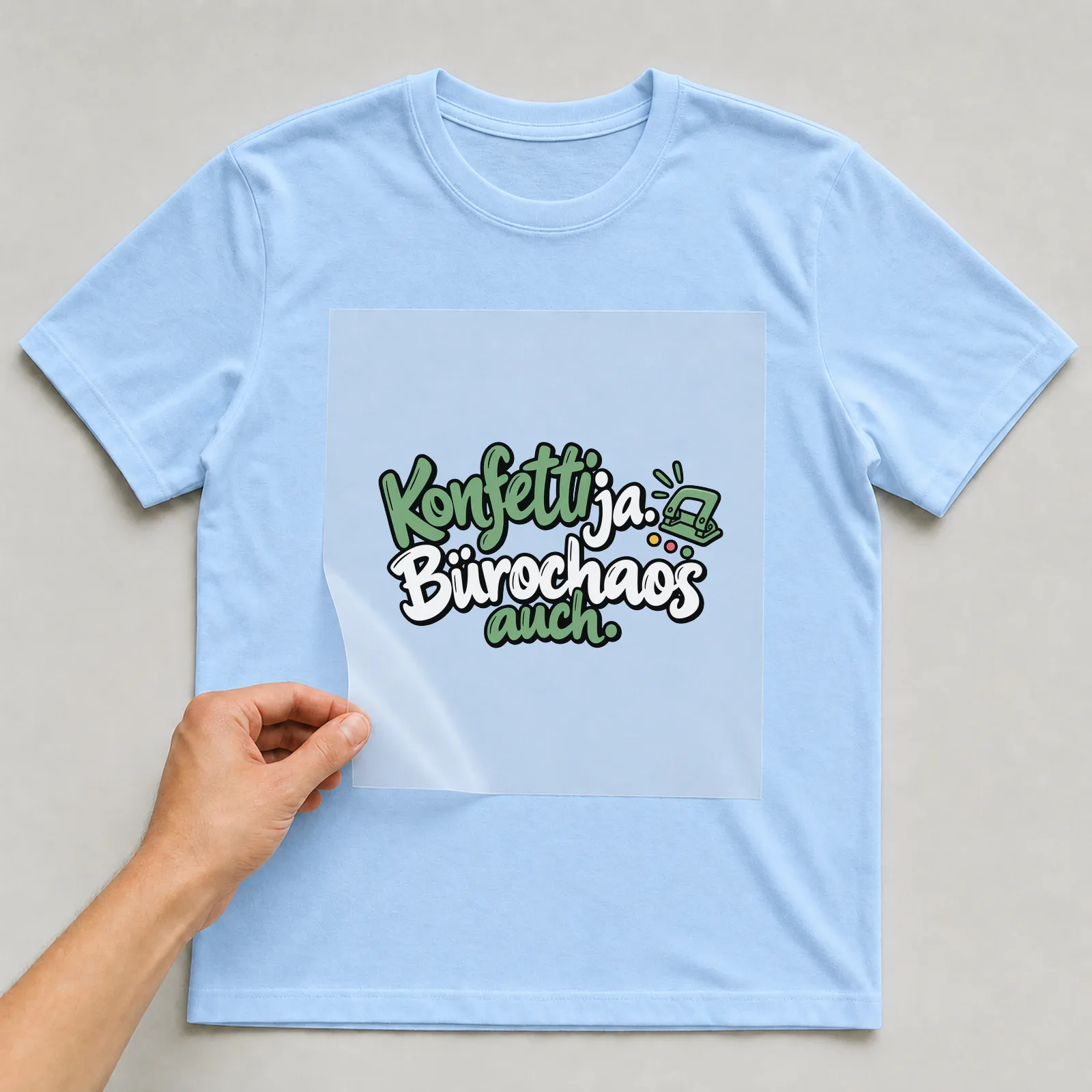 Bügelbild „Konfetti ja. Bürochaos auch.“ auf hellblauem T-Shirt, Folie wird aufgelegt