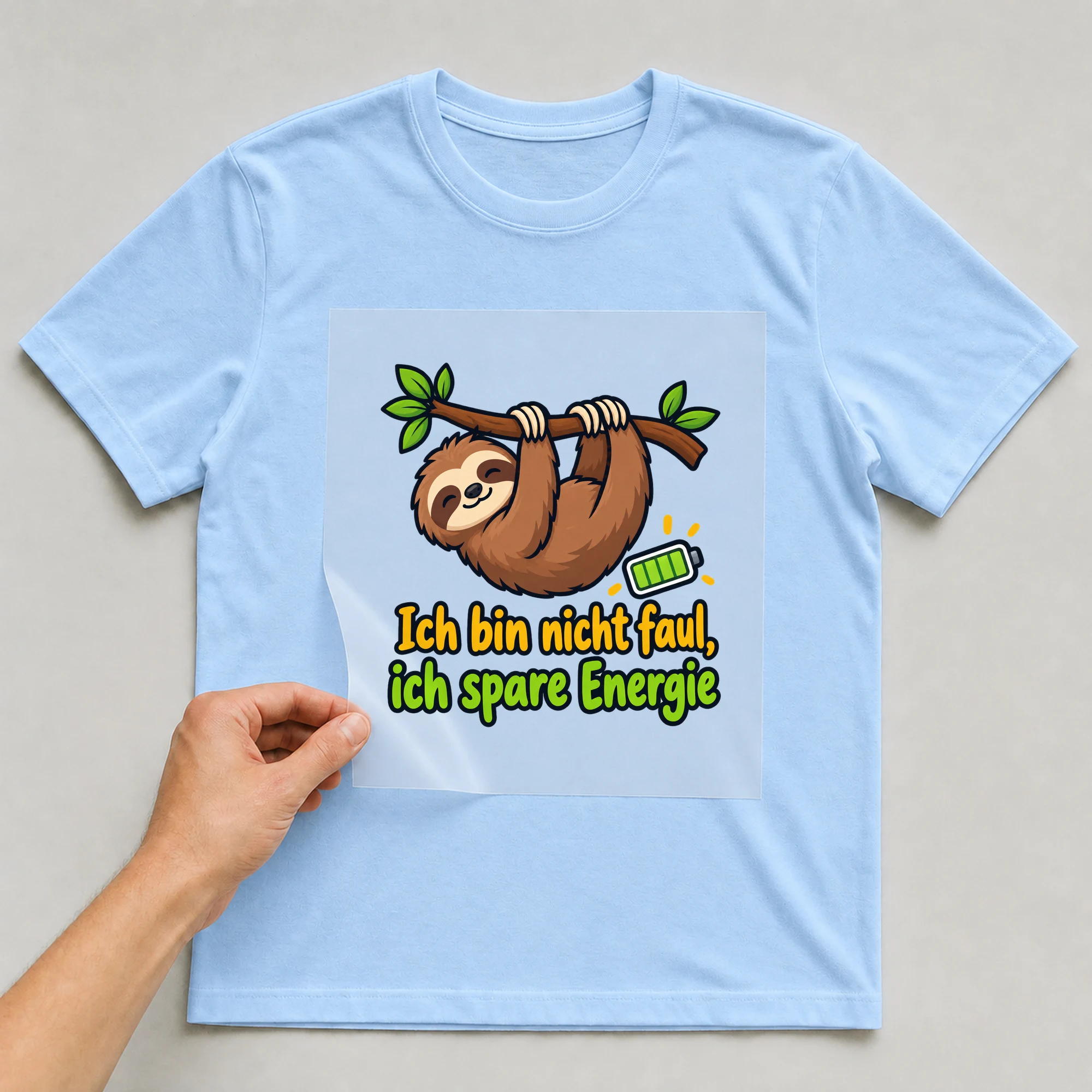 Bügelbild „Ich bin nicht faul, ich spare Energie“ auf babyblauem T-Shirt, Folie wird aufgelegt